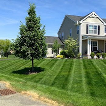 A large gray house with white trim and a front porch, surrounded by a well-maintained lawn with striped grass and a small tree in front.
