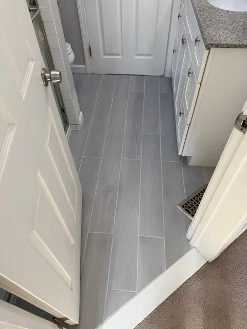 A small bathroom or laundry room with light gray tiled flooring, white cabinetry, and a white door.