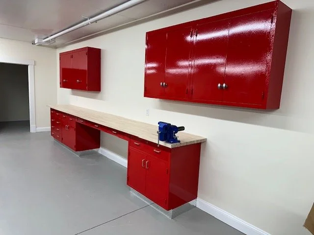 Workshop with red cabinets, a beige workbench, and a blue vise, in a room with white walls and gray flooring.