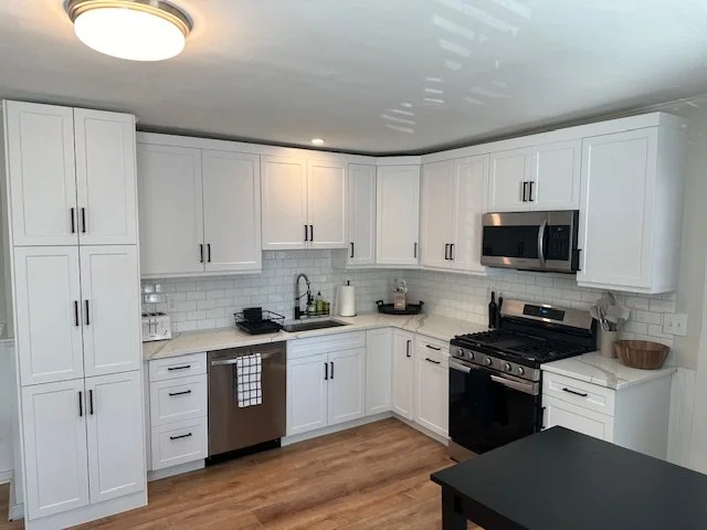 Modern white kitchen with stainless steel appliances, white cabinetry, subway tile backsplash, and wood flooring.