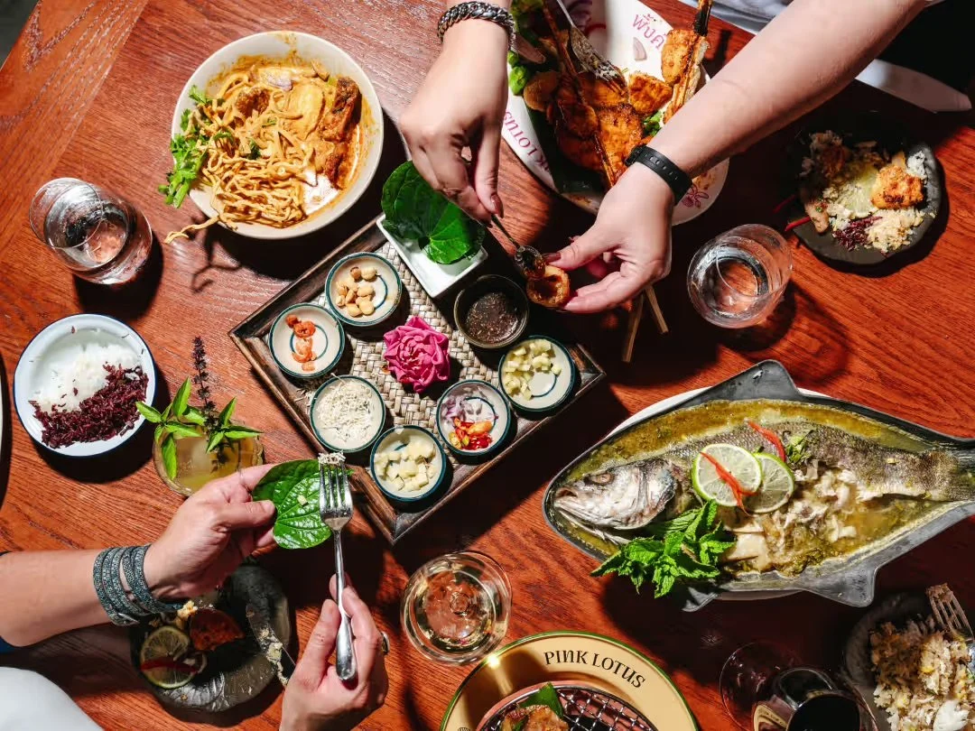 Overhead dinner spread at Pink Lotus Thai Restaurant featuring whole branzino, miang kham, cocktails, noodles, and shareable Thai dishes in Atlanta