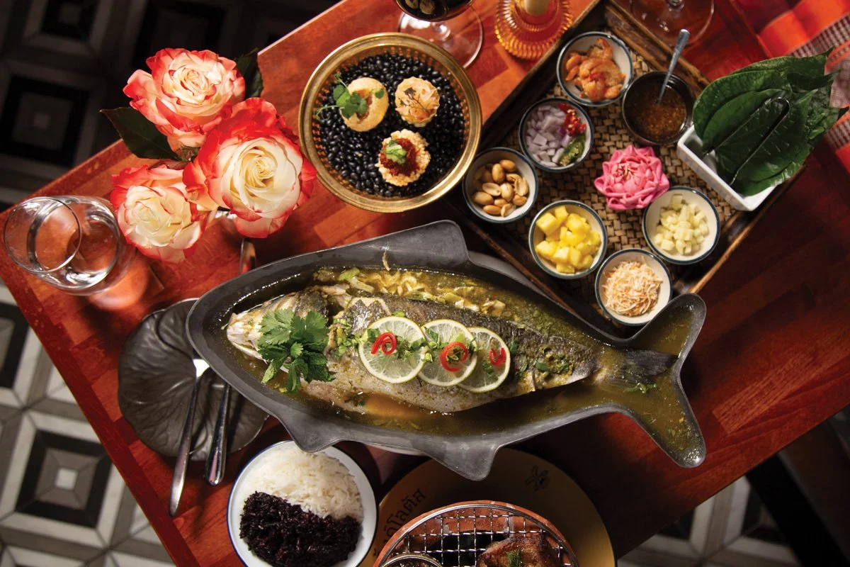 Overhead spread at Pink Lotus Thai Restaurant featuring whole branzino, miang kham ingredients, Thai dishes, and colorful table presentation in Atlanta