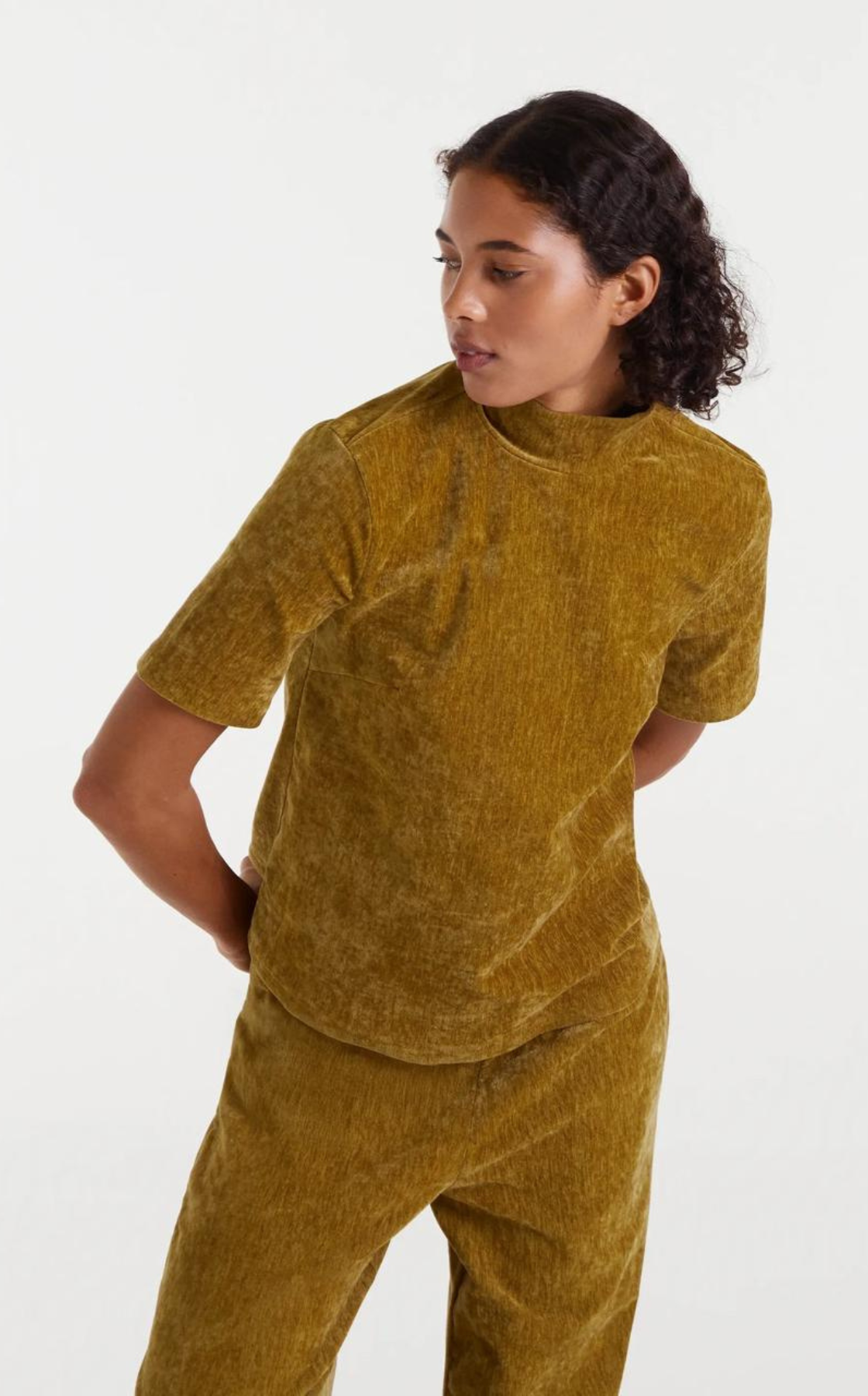 A woman wearing a matching mustard yellow velvety T-shirt and pants, looking to her left against a plain white background.