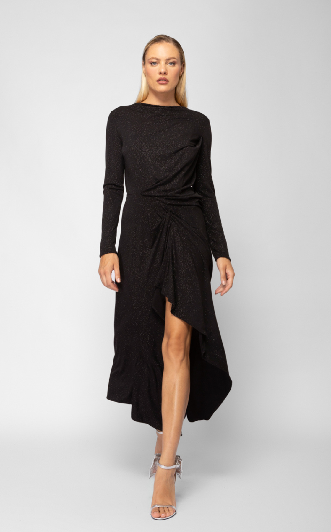 A woman walking in a black dress with a thigh-high slit and silver high heels.