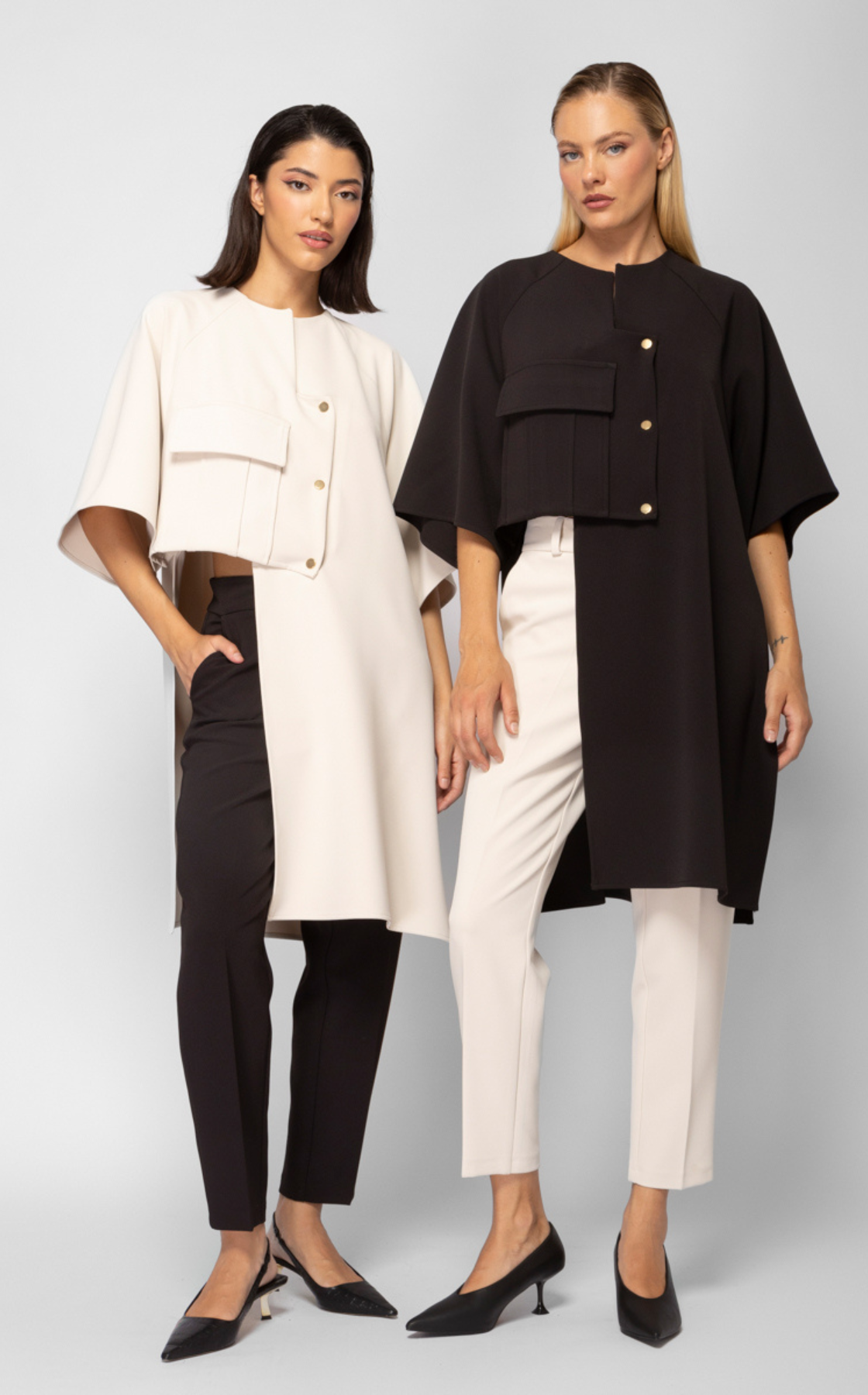 Two women in stylish black and white outfits standing against a plain backdrop.