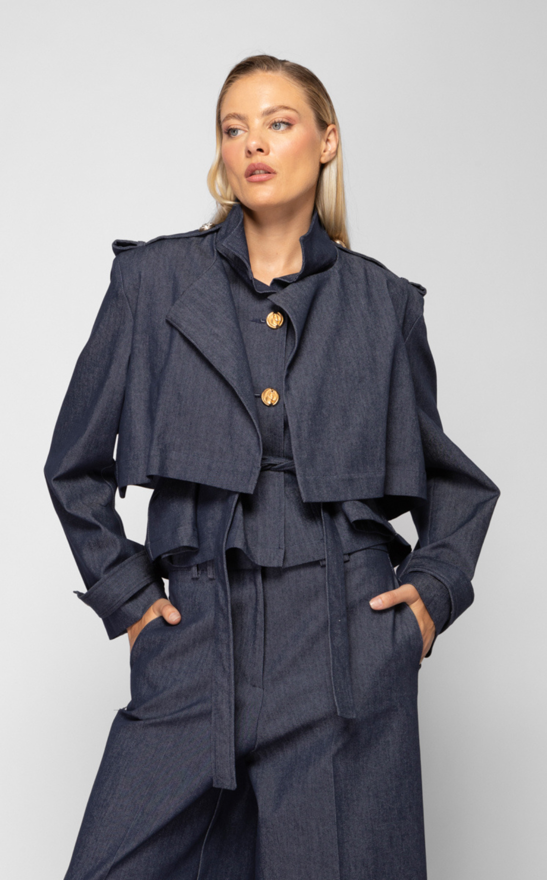 A woman wearing a dark blue denim cropped jacket and matching loose-fitting pants with hands in pockets.