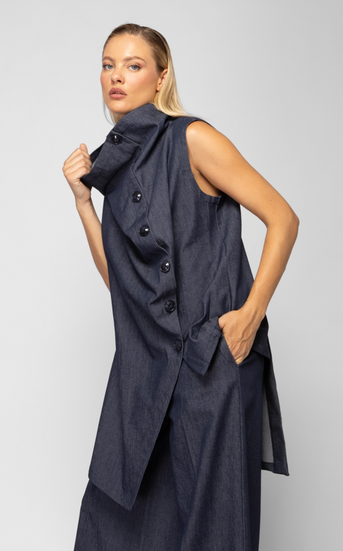 A woman wearing a sleeveless denim vest with buttons and matching wide-leg denim pants, standing against a plain background.