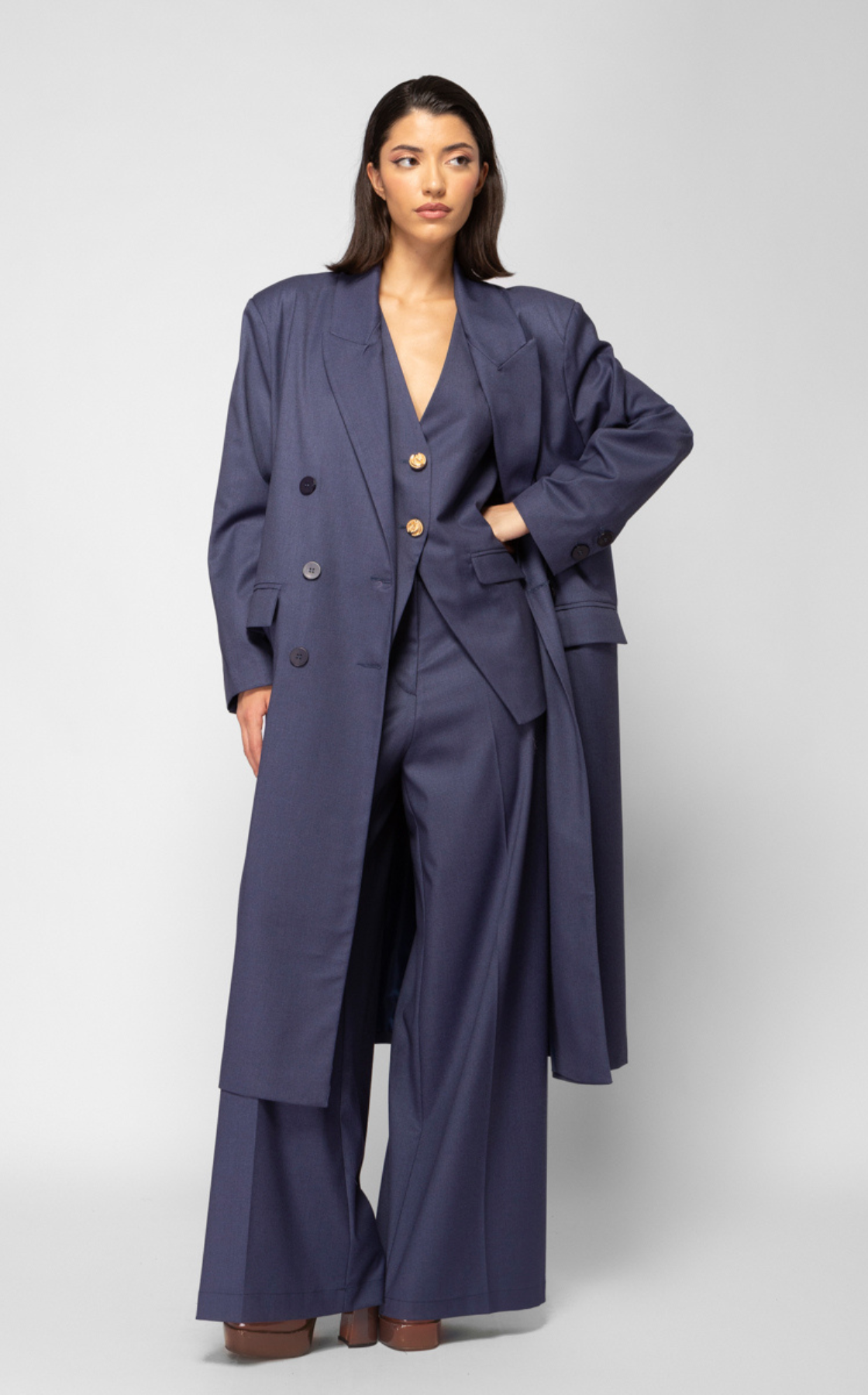 A woman wearing a navy blue blazer and matching wide-leg trousers standing against a light gray background.