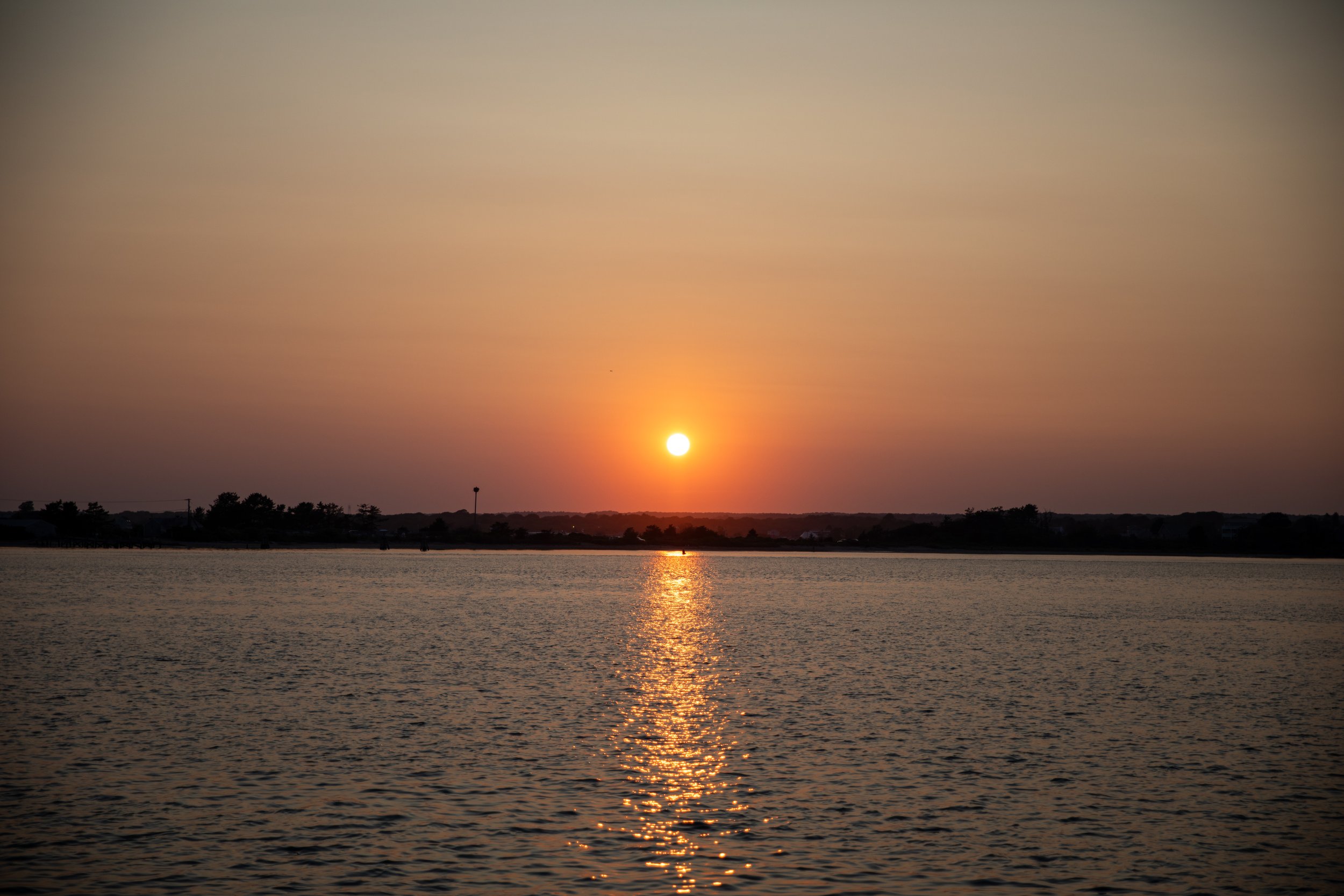 Sunset over a calm lake with an orange sky and dark shoreline silhouette.