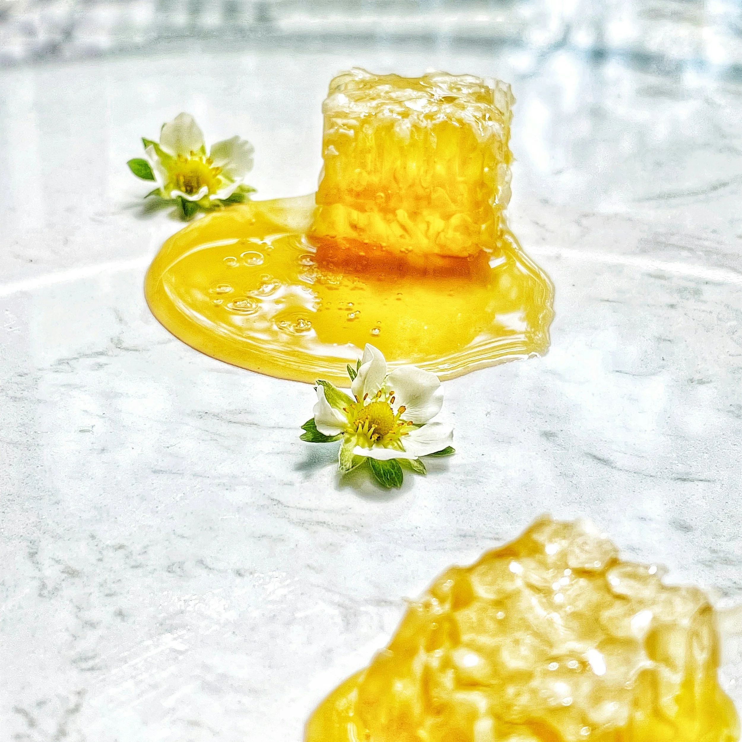Honeycomb with honey dripping on a white surface, accompanied by small white flowers.