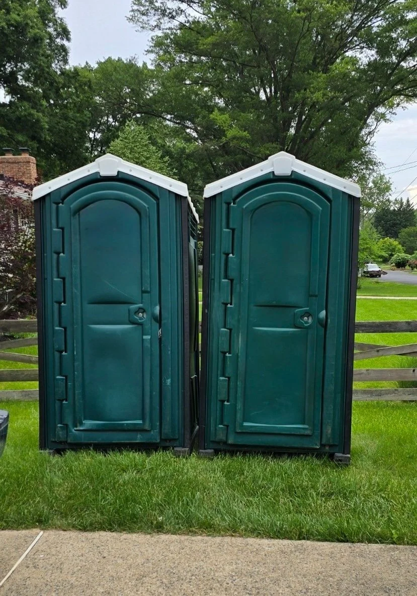 Two green standard portable restrooms from Neptune Purity Stations placed on a grassy residential lawn, ready for use at a local DMV (Washington DC, Maryland, and Virginia) area event or job site.
