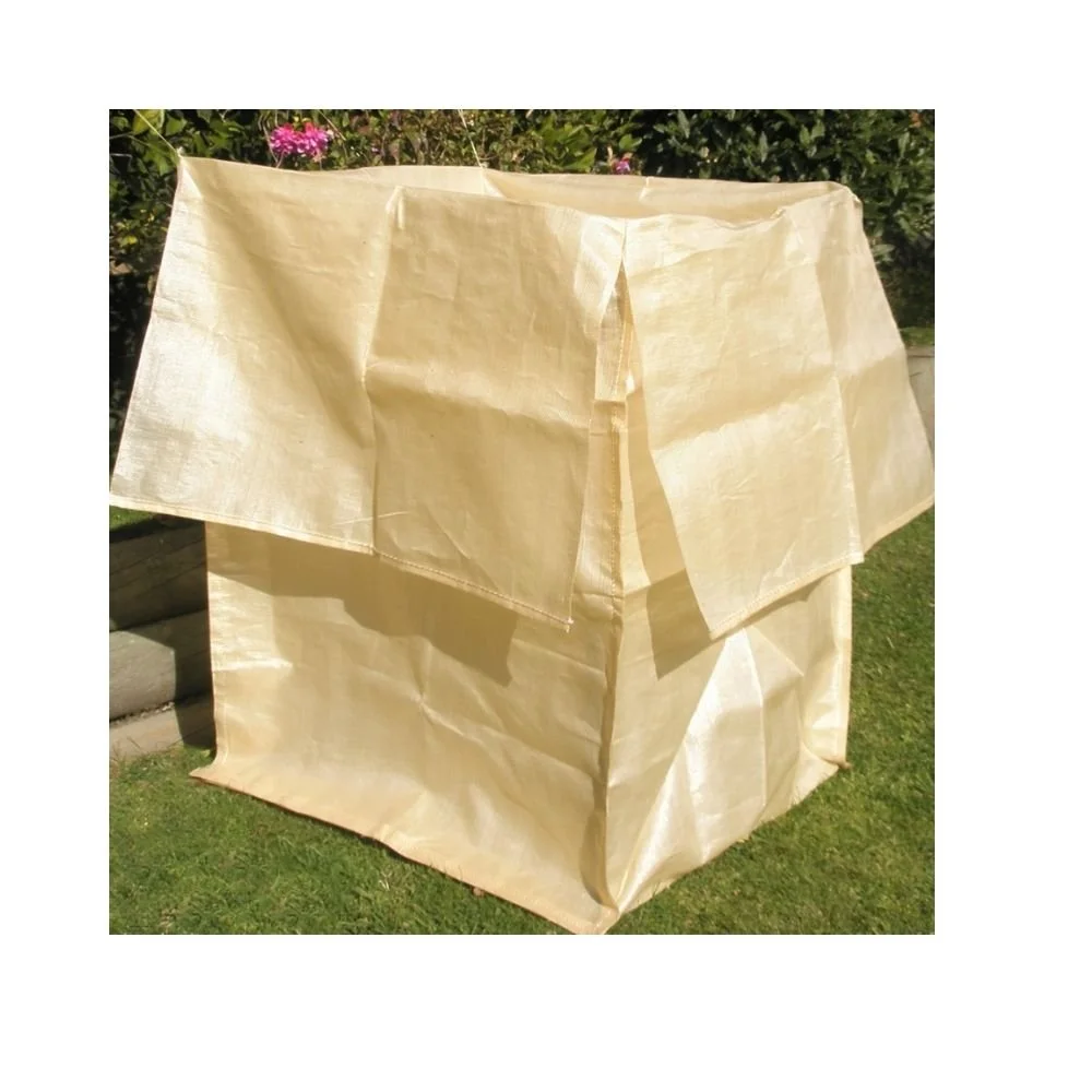 A large beige fabric object resembling a tent or makeshift shelter set up outdoors on grass, with a garden and flowers in the background.