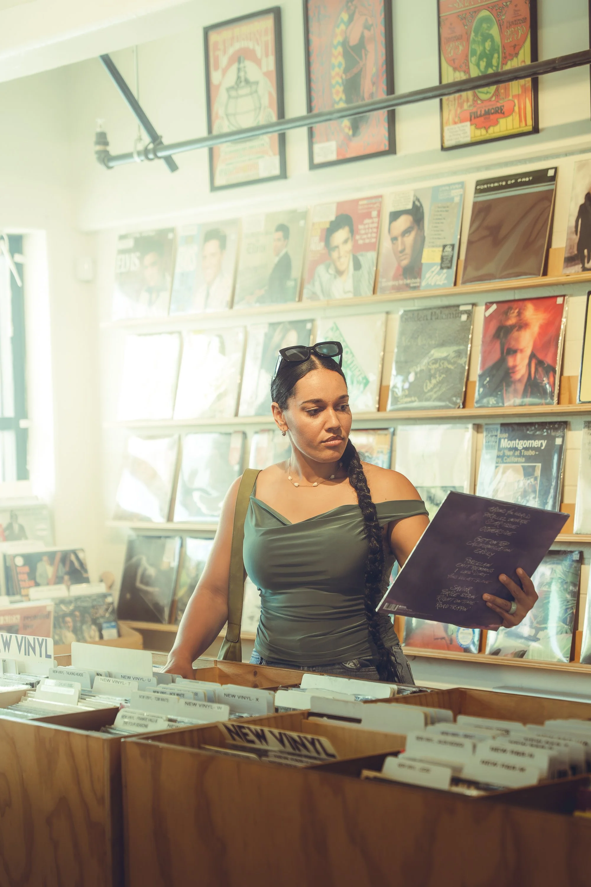 A woman shopping in a record store, looking at vinyl records with album covers displayed on shelves behind her.