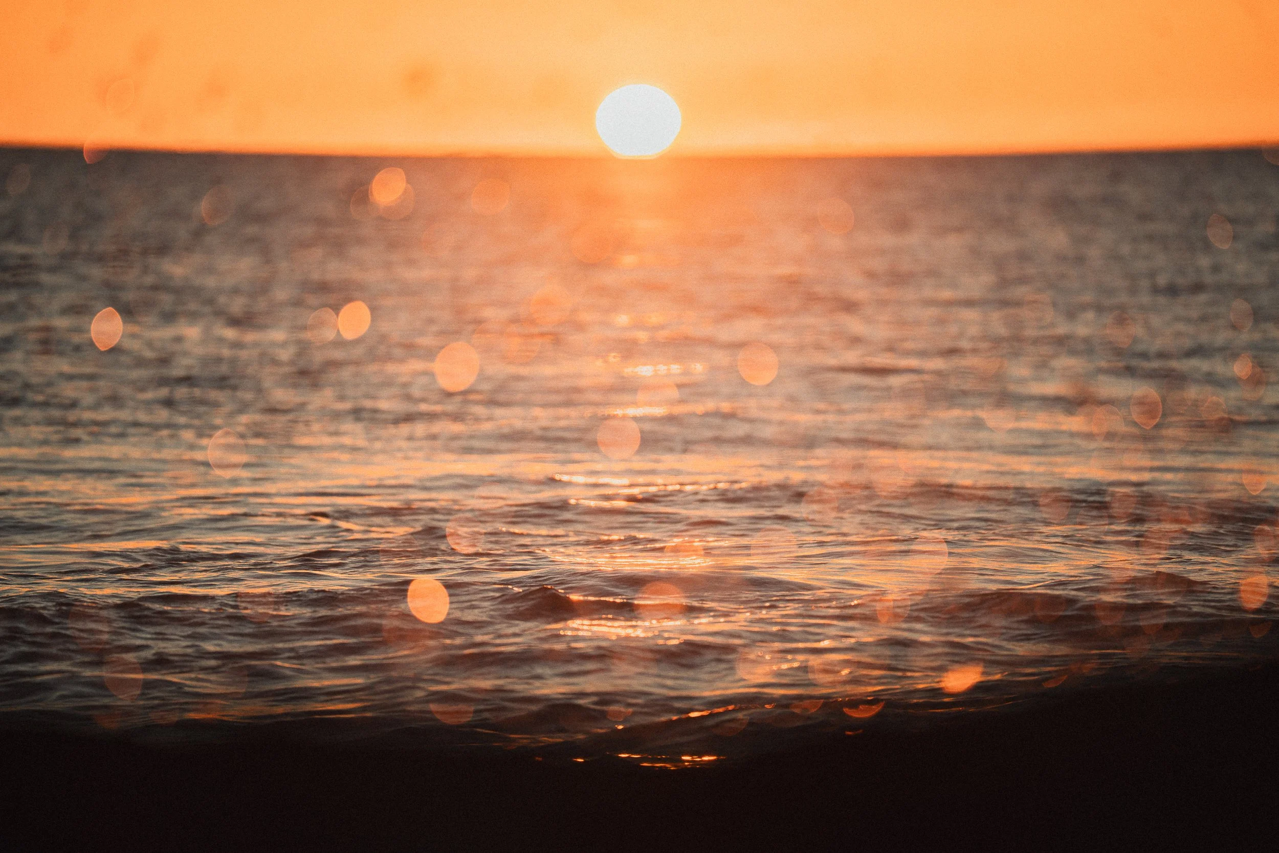 Sunset over the ocean with orange and pink sky and water reflecting the sunlight.