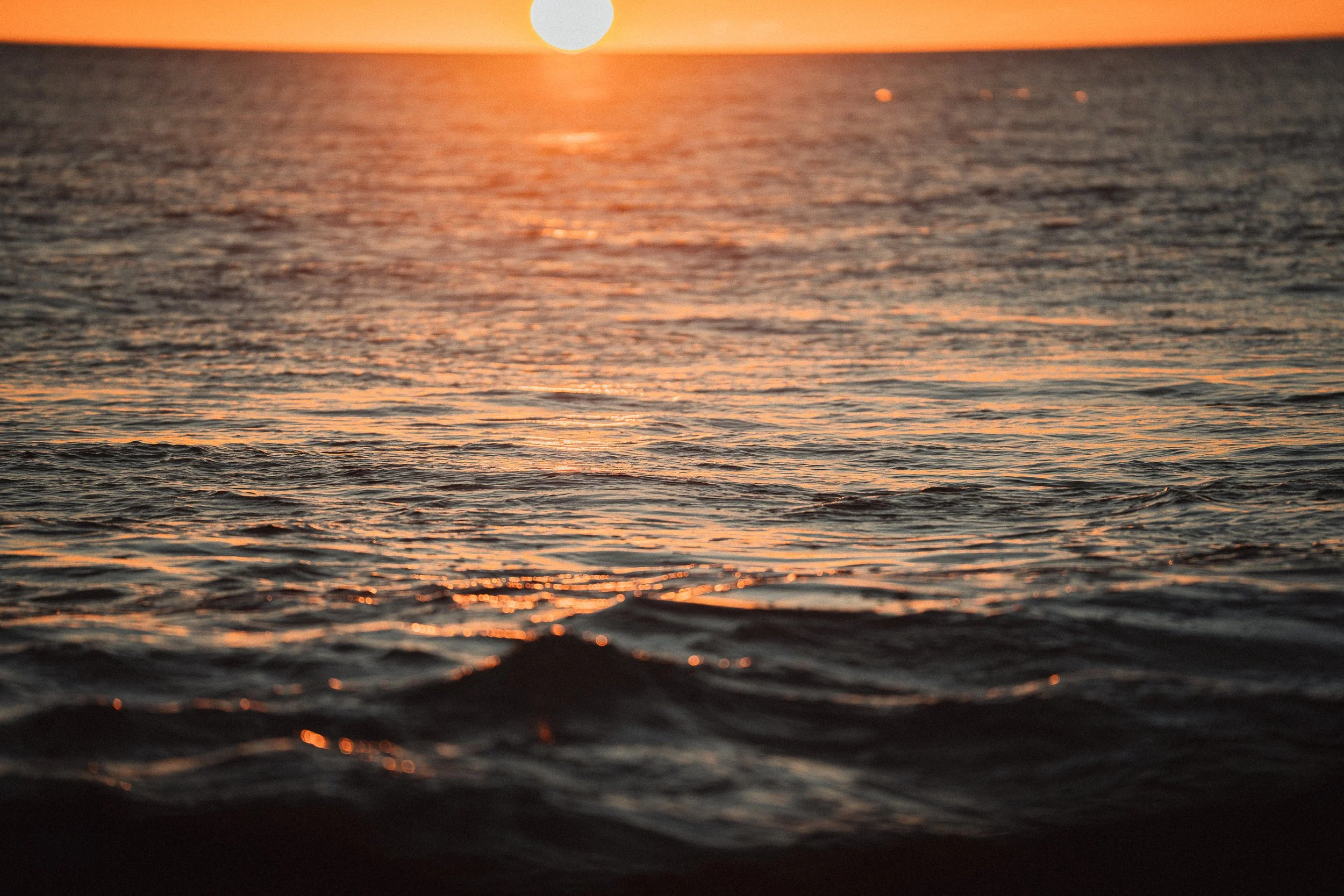 Sunset over the ocean with the sun near the horizon and calm rippling water.