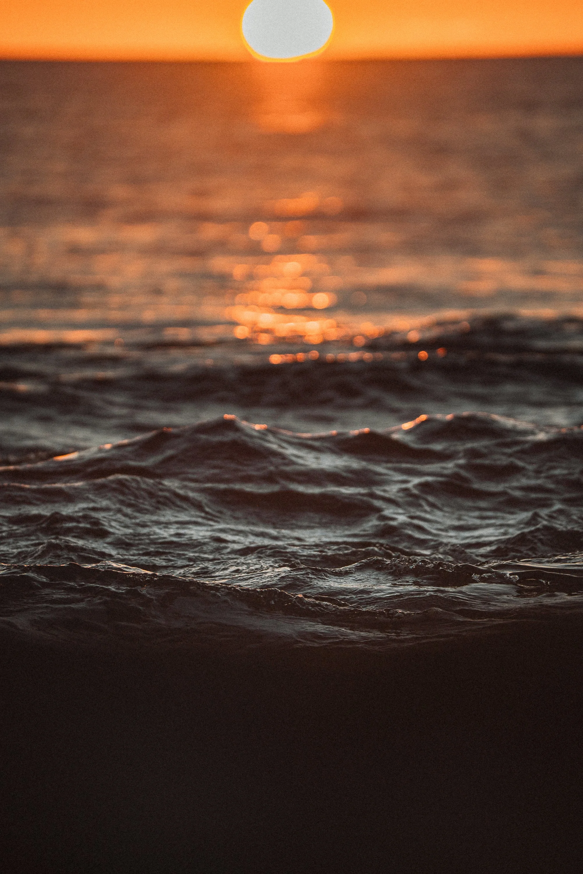 Sun setting over the ocean with waves in the foreground and orange, pink, and yellow sky.