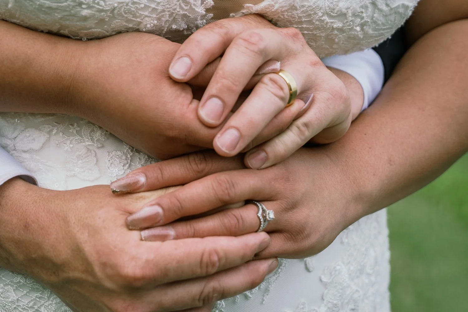 A close-up of two couples holding their hands together, focusing on the wedding rings on their fingers.