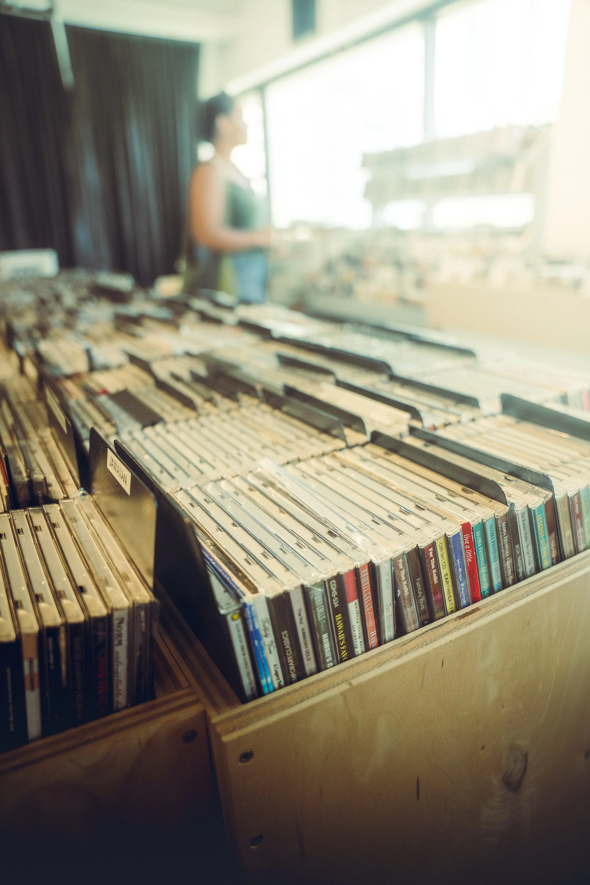 Blurry photo of a person standing near a large window with a display of books or magazines in the foreground inside a store or library.