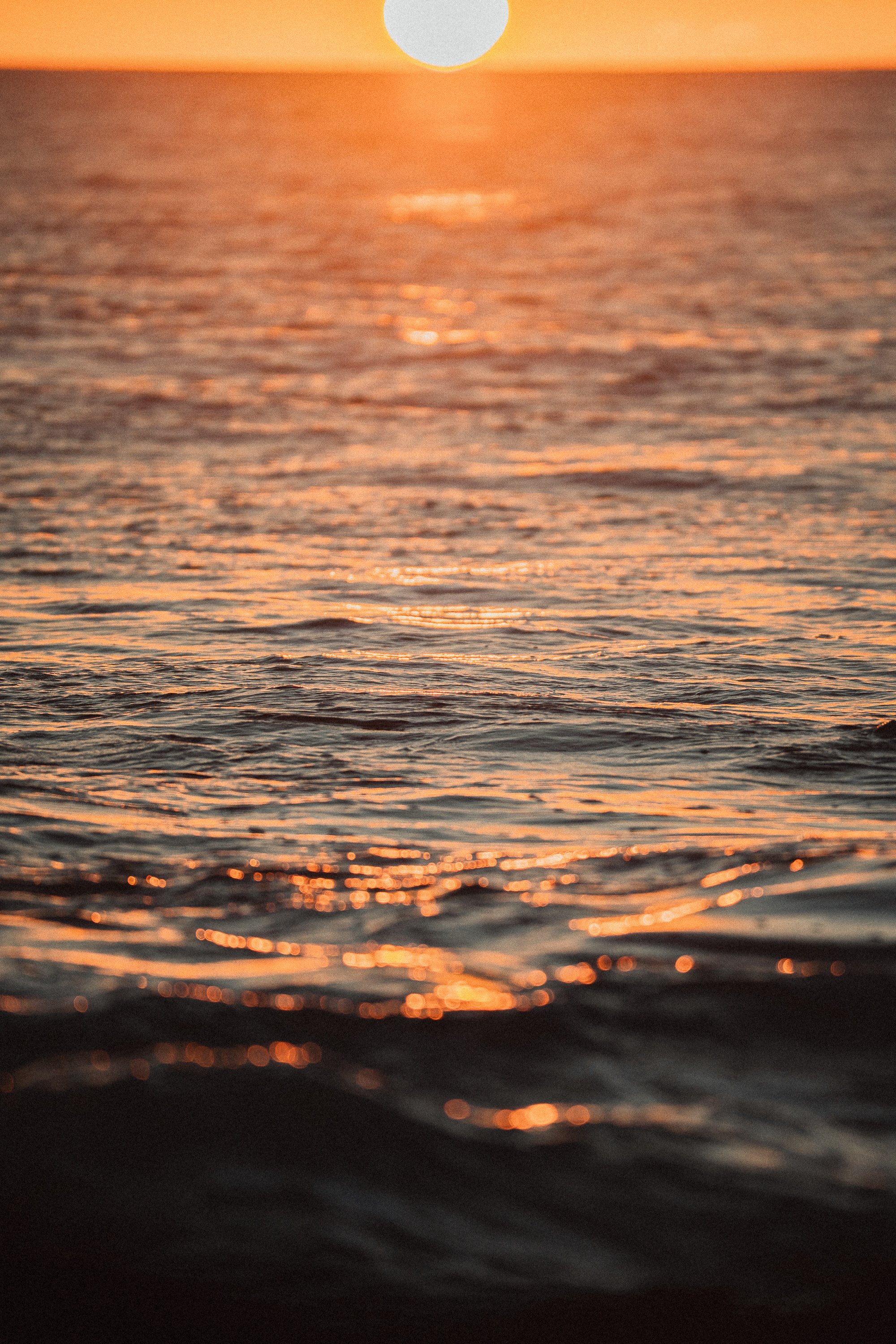Sunset over the ocean with the sun near the horizon, casting orange and pink reflections on the water.