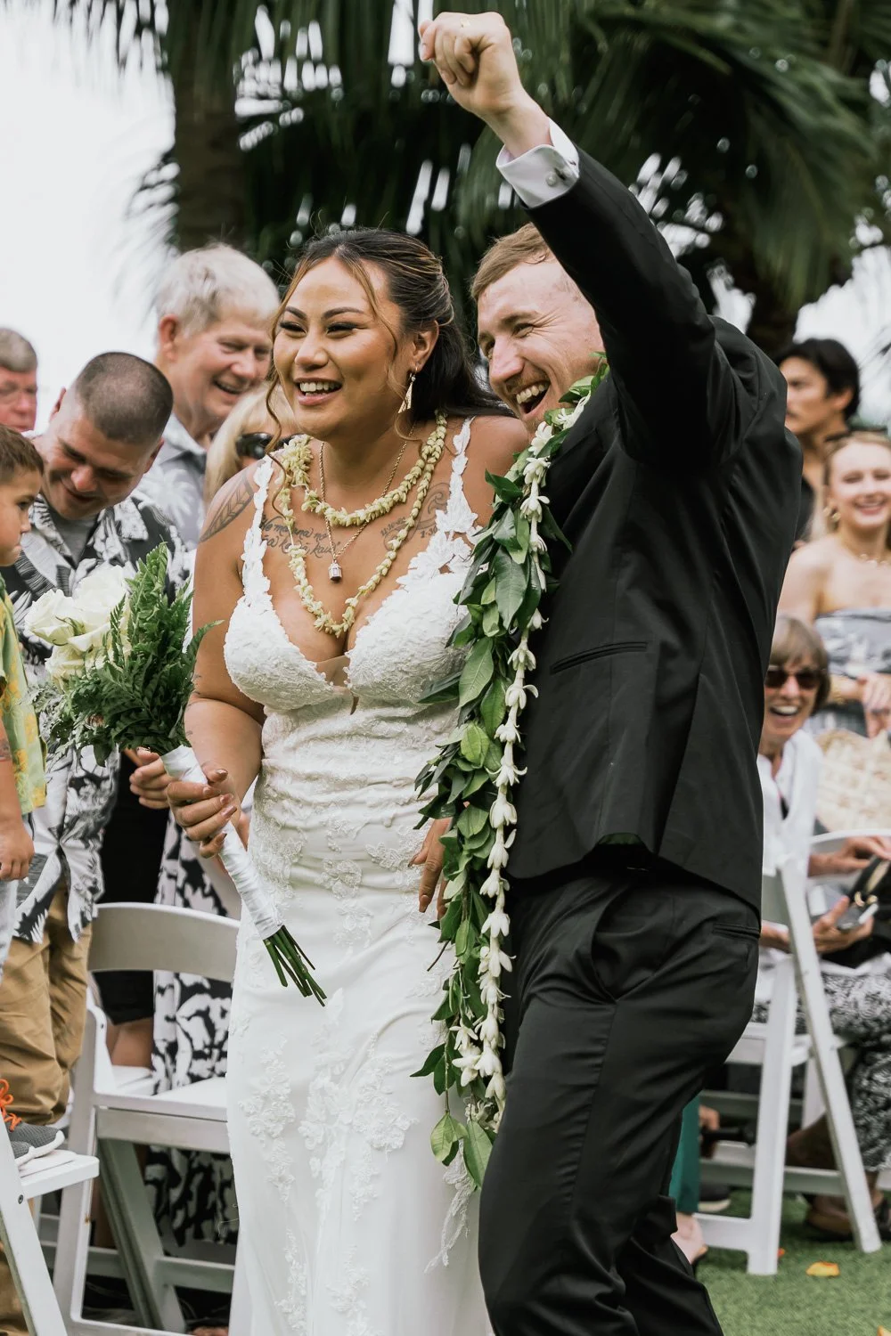 A bride and groom celebrating at their wedding ceremony, surrounded by friends and family outdoors, with the groom raising his fist in celebration.