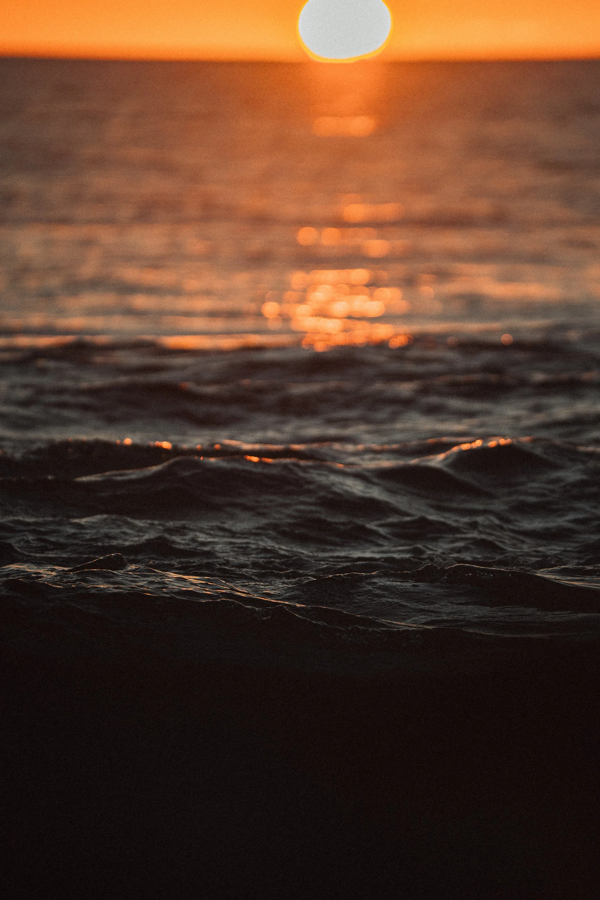 Close-up of ocean waves during sunset with an orange sky and the sun reflecting on the water's surface.