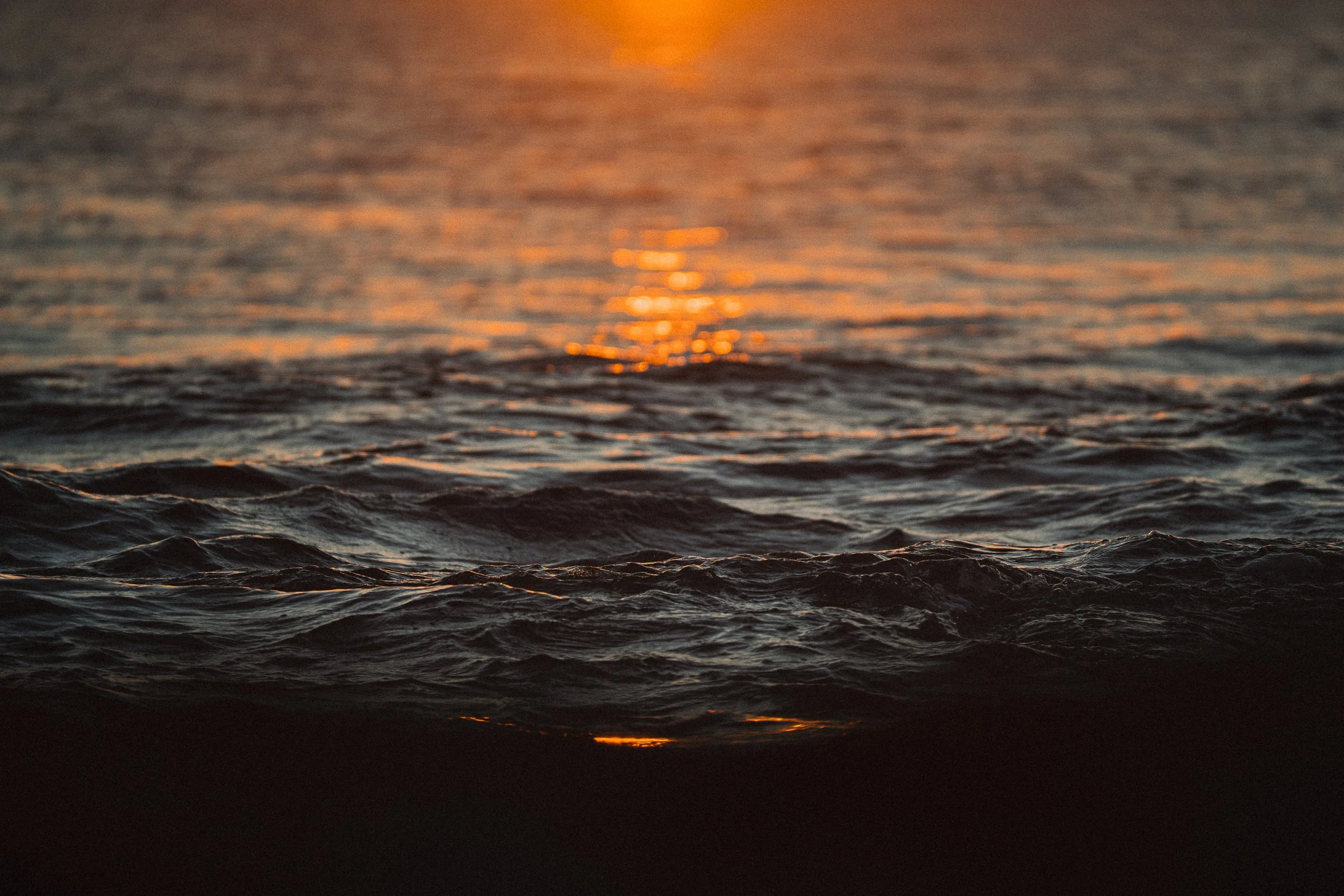 Close-up of the ocean at sunset with gentle waves and orange sunlight reflection on the water