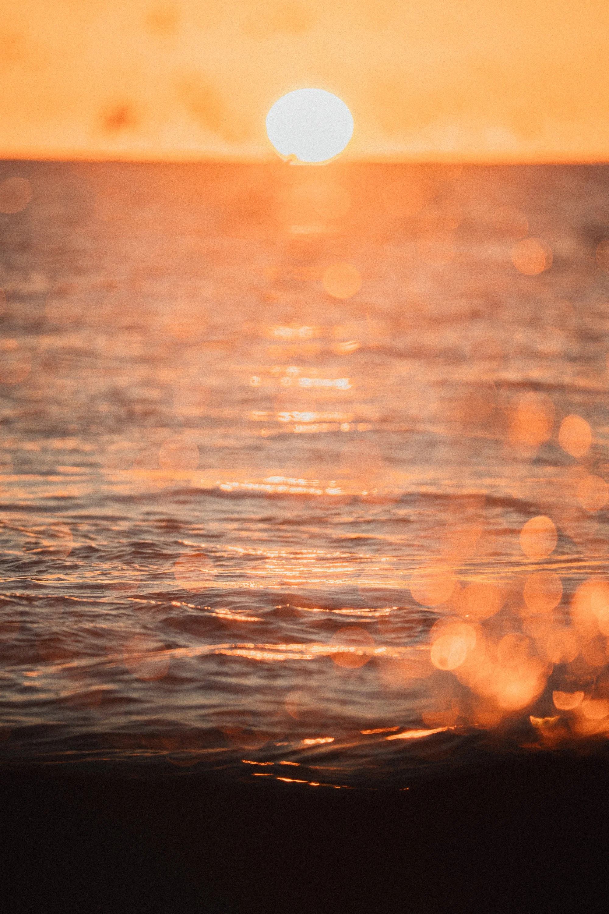 Sunset over the ocean with the sun near the horizon and reflections on the water.