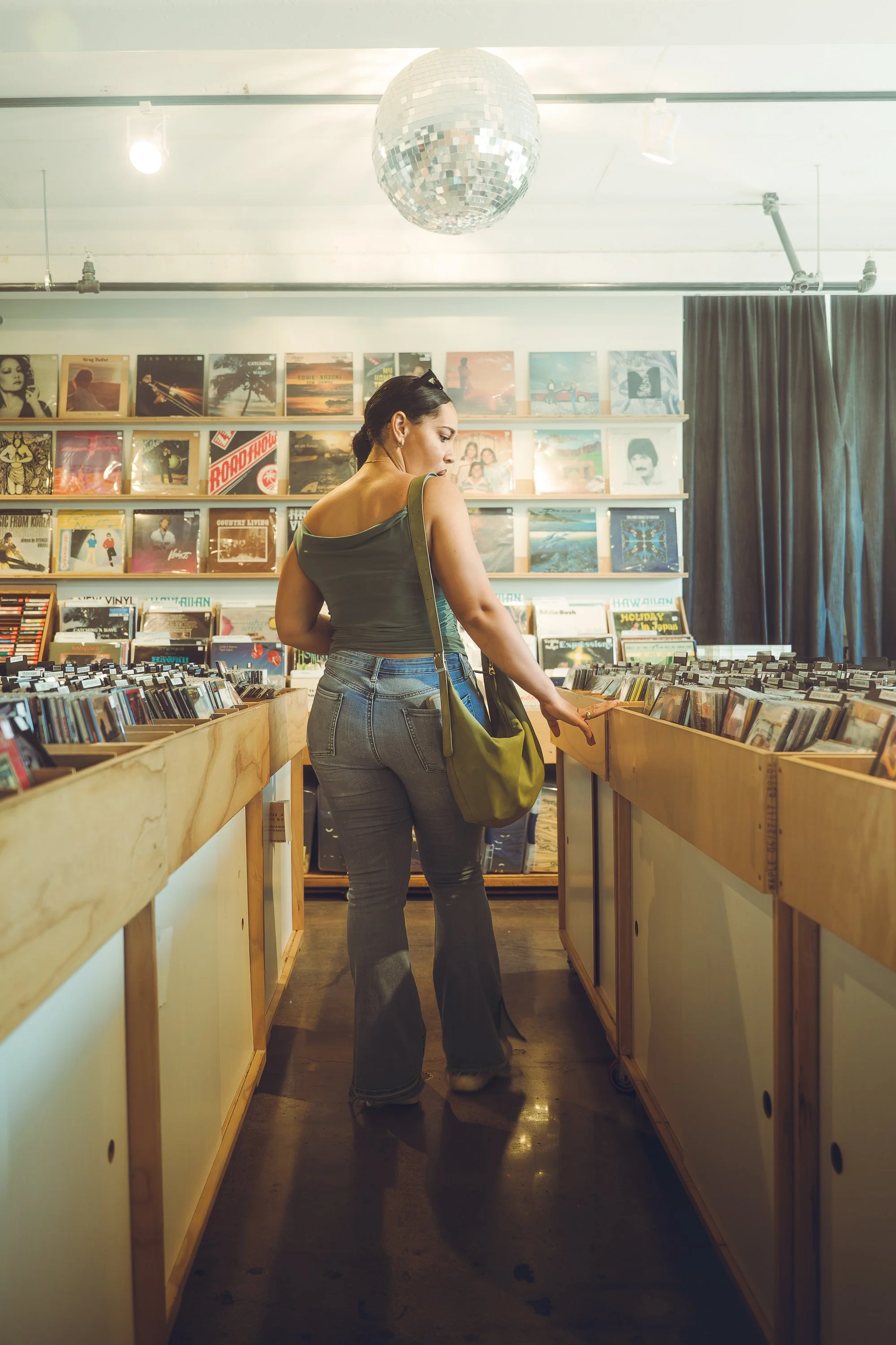 A woman browsing vinyl records in a record store, with records displayed behind her and a disco ball hanging from the ceiling.
