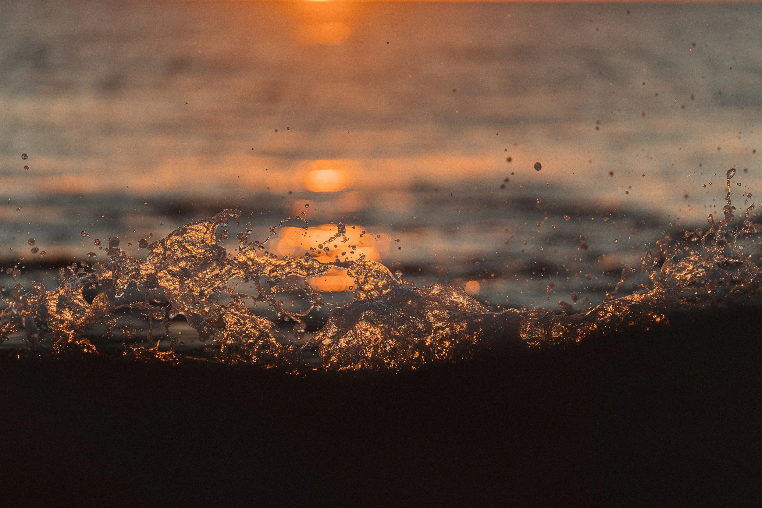 Sunset over the ocean with waves splashing.
