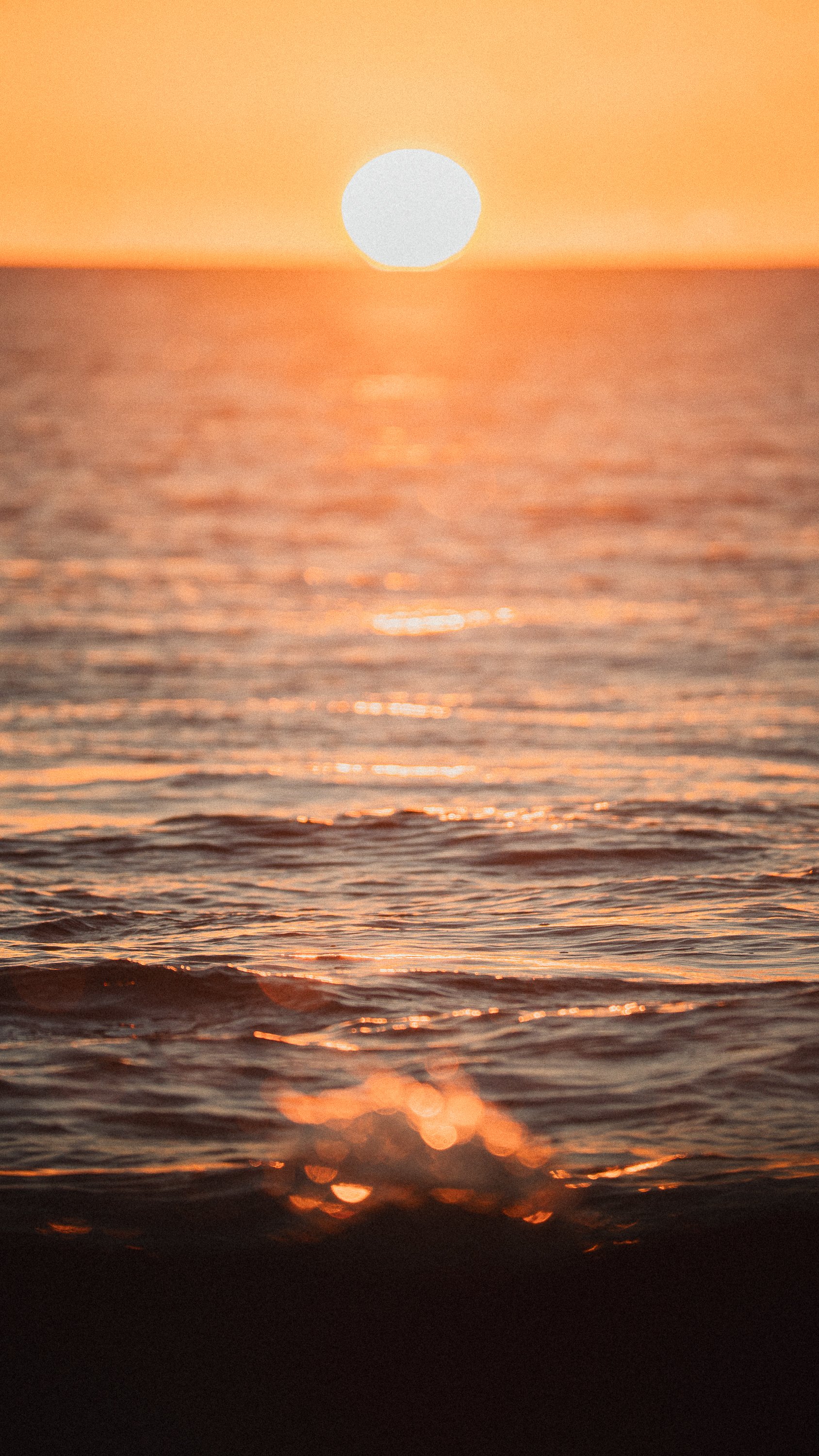 Sunset over the ocean with orange sky and reflections on the water.