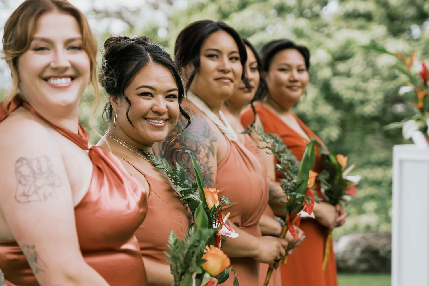 Group of five women in peach-colored dresses holding flowers during outdoor wedding ceremony