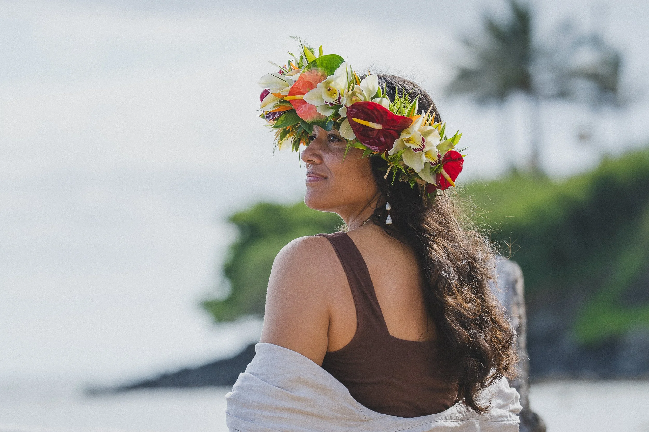 A woman wearing a floral crown made of various colorful flowers, looking to the side with a serene expression.