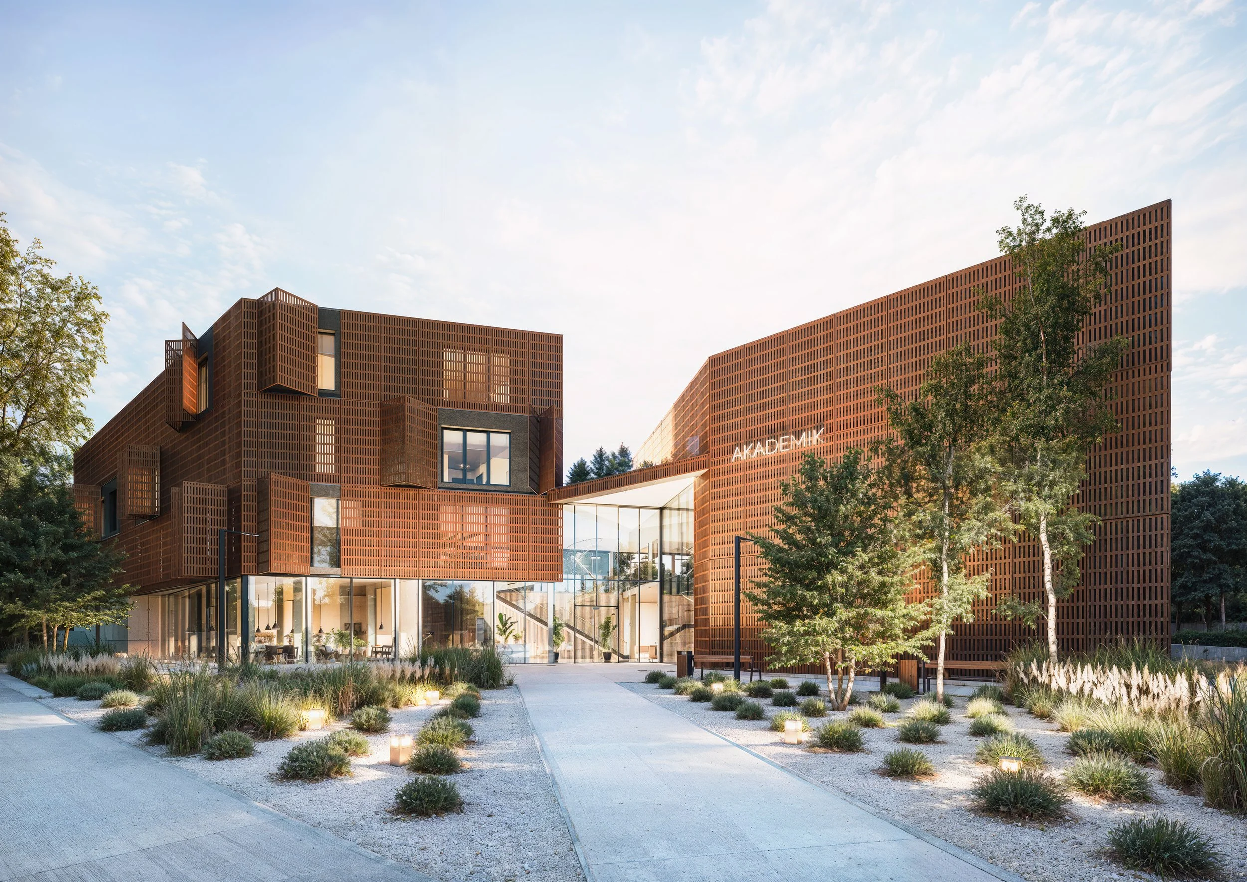 Modern building with a perforated exterior, large glass entrance, surrounded by trees and landscaped garden. Kamil Rombczyk portfolio architectural vizualization. Kamil Rombczyk portfolio architectural vizualization. Kamil Rombczyk portfolio wizualiz