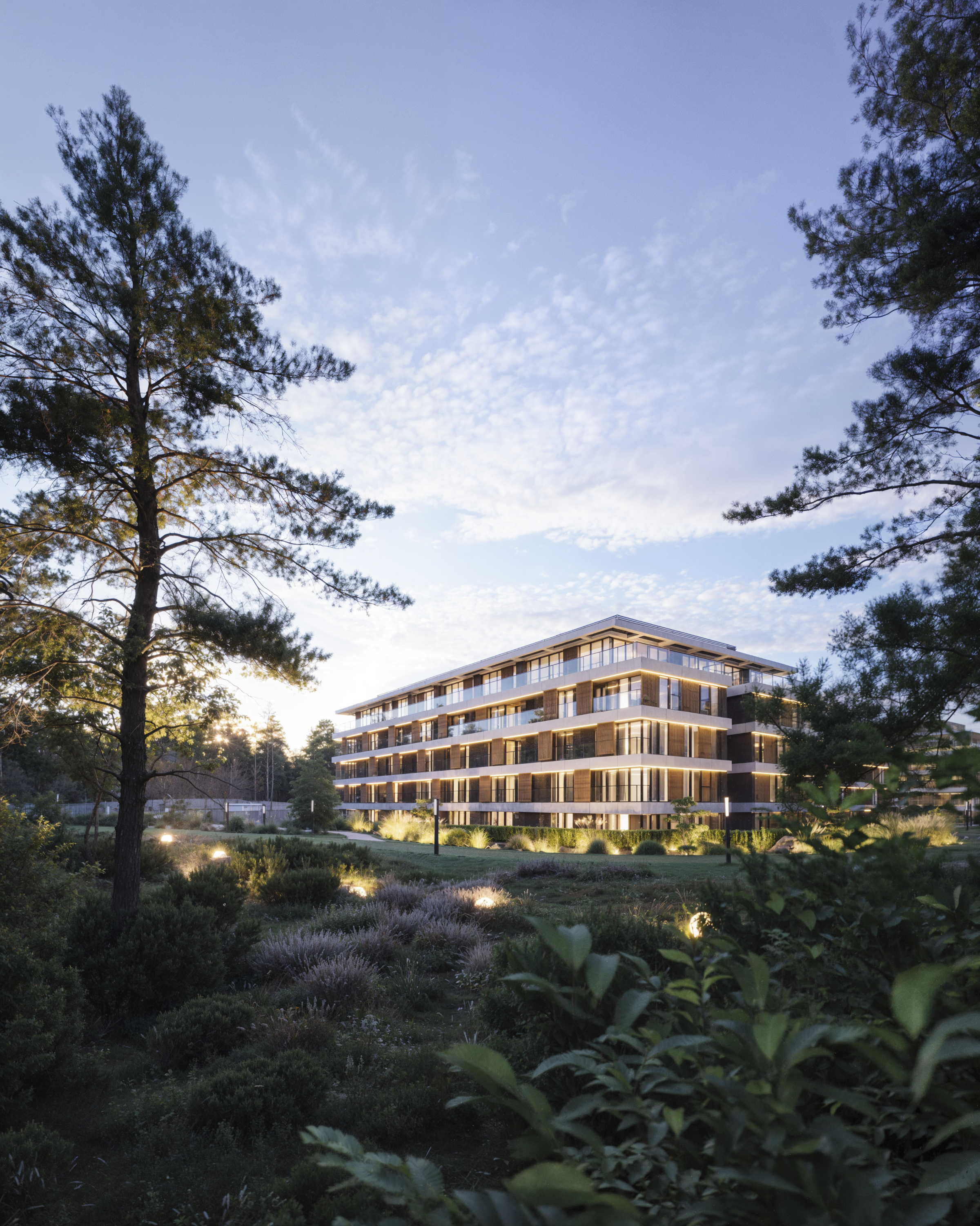 Modern multi-story apartment building at dusk, surrounded by trees and landscaped gardens with pathway lighting. Kamil Rombczyk portfolio architectural vizualization. Kamil Rombczyk portfolio architectural vizualization. Kamil Rombczyk portfolio wizu