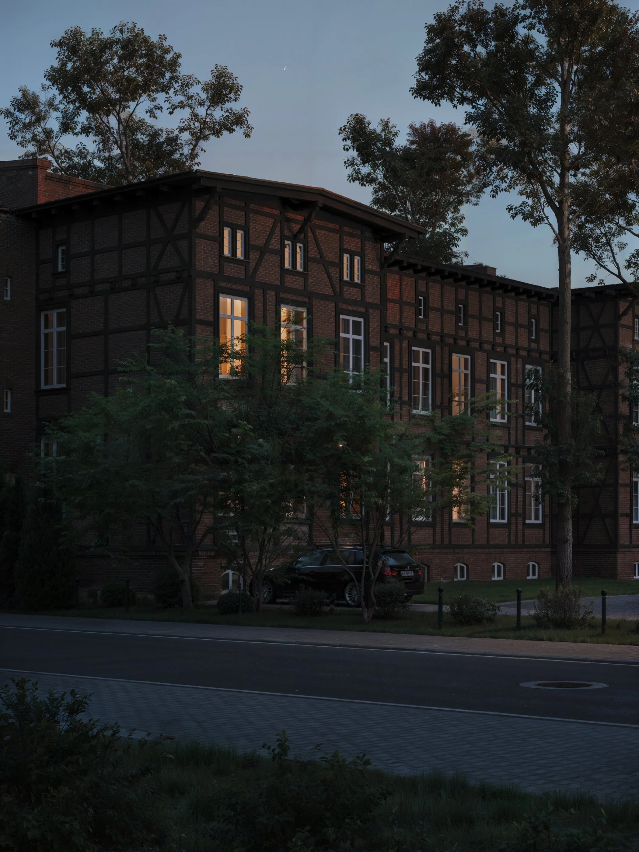 A multi-story brick building with exposed wooden beams and several illuminated windows at dusk, surrounded by trees and parked cars. Kamil Rombczyk portfolio architectural vizualization. Kamil Rombczyk portfolio wizualizacje architektoniczne. Wizuali