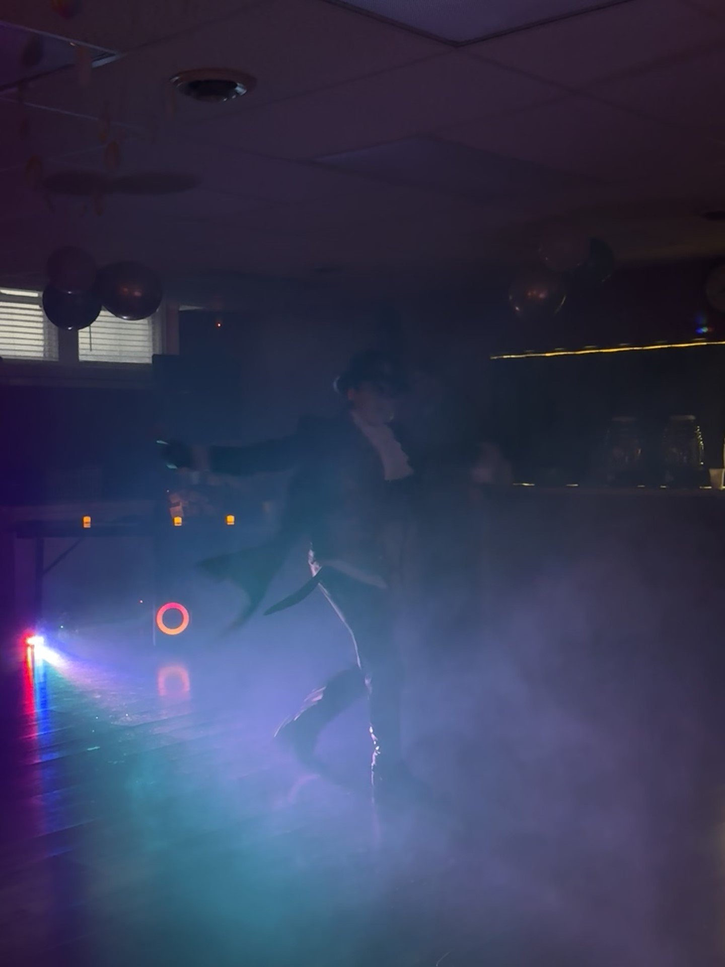 Person dancing in a foggy room with dim lighting and colorful spotlights