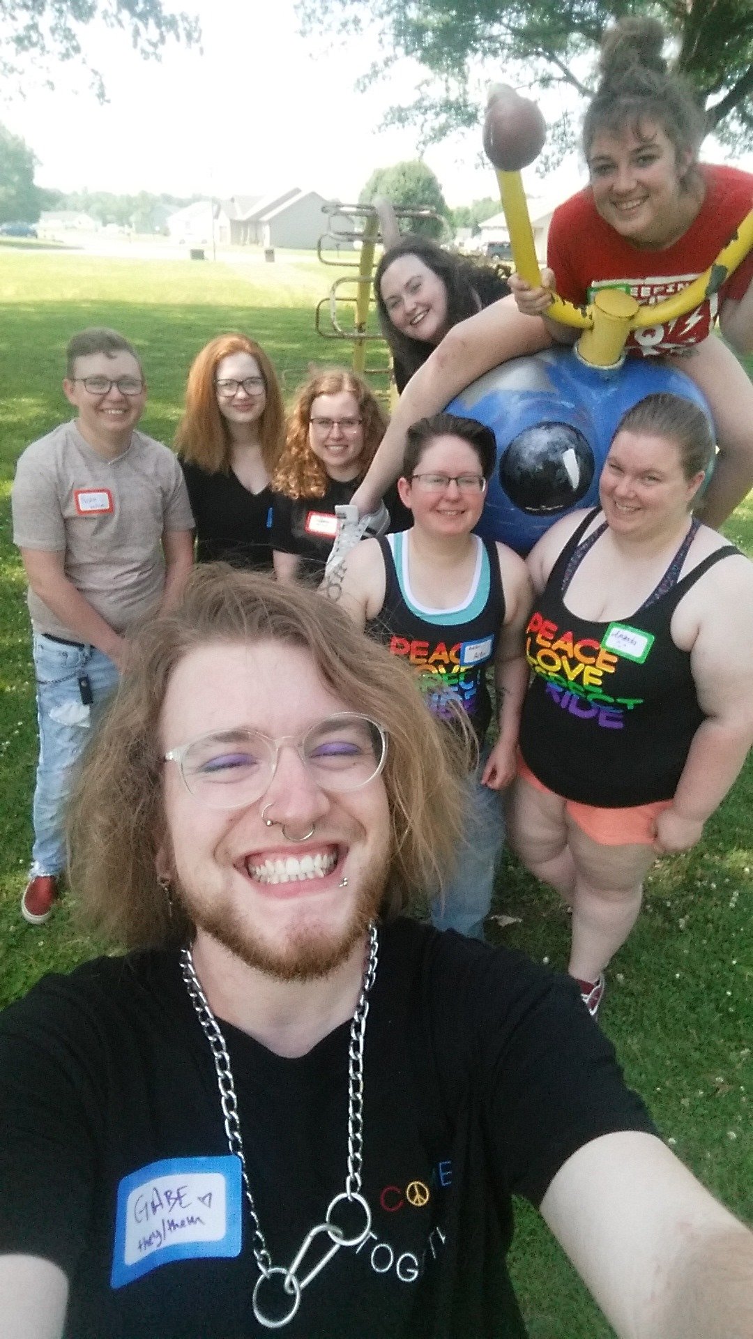 Group of seven people smiling in a park with play equipment in the background.