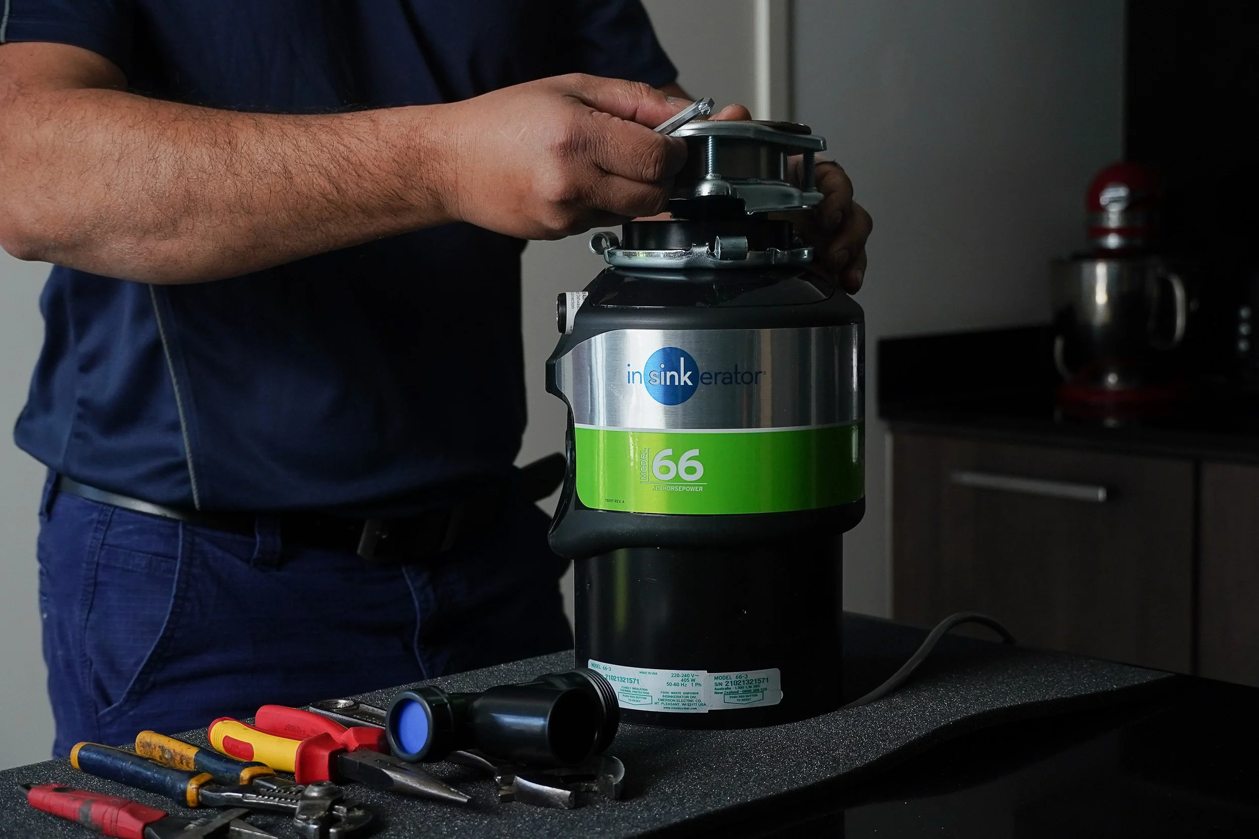 Person assembling or installing an InSinkErator garbage disposal with tools on a counter.