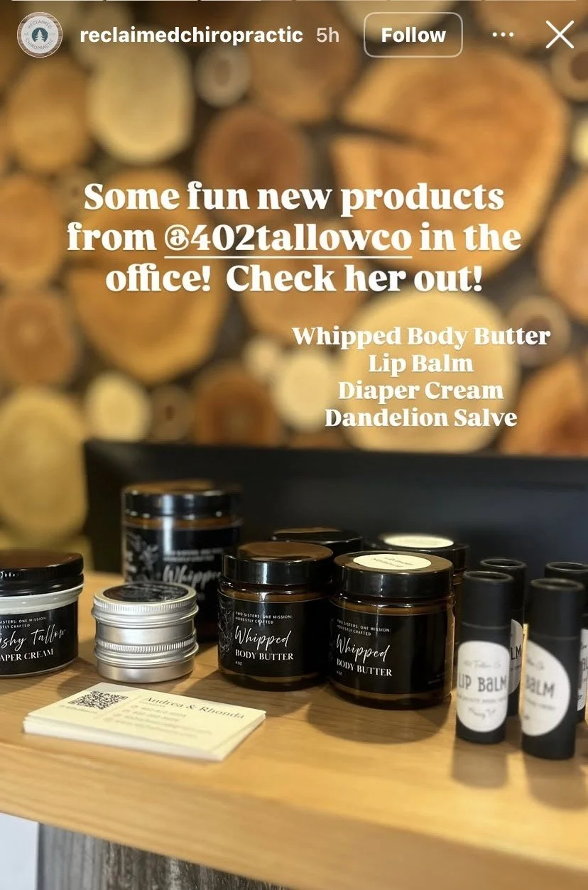 Various natural skincare products on a wooden table, including whipped body butter, lip balm, and diaper cream, with a blurred background of wood logs.