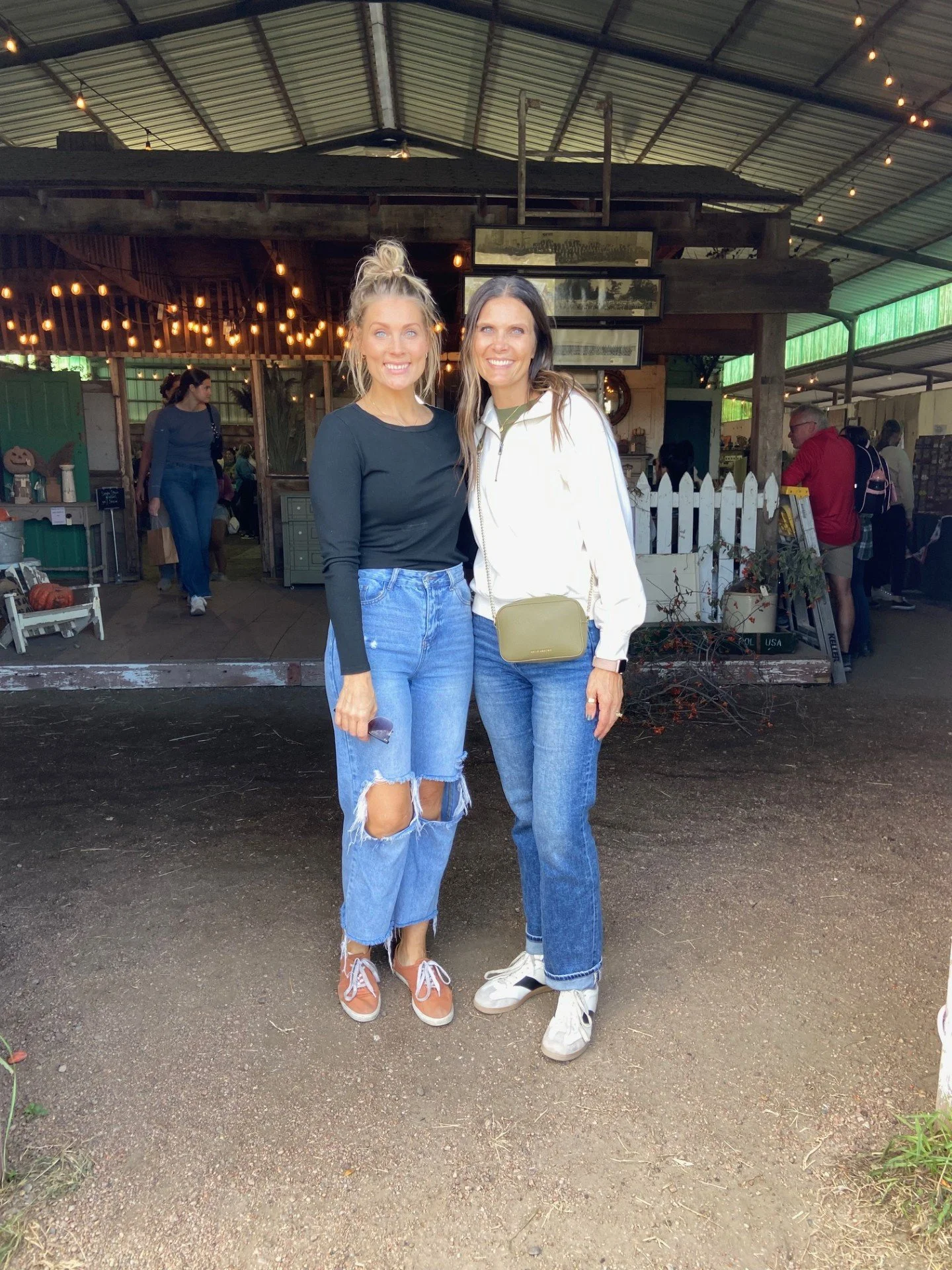 Two women standing together inside a rustic venue with string lights and wooden decor, smiling at the camera.