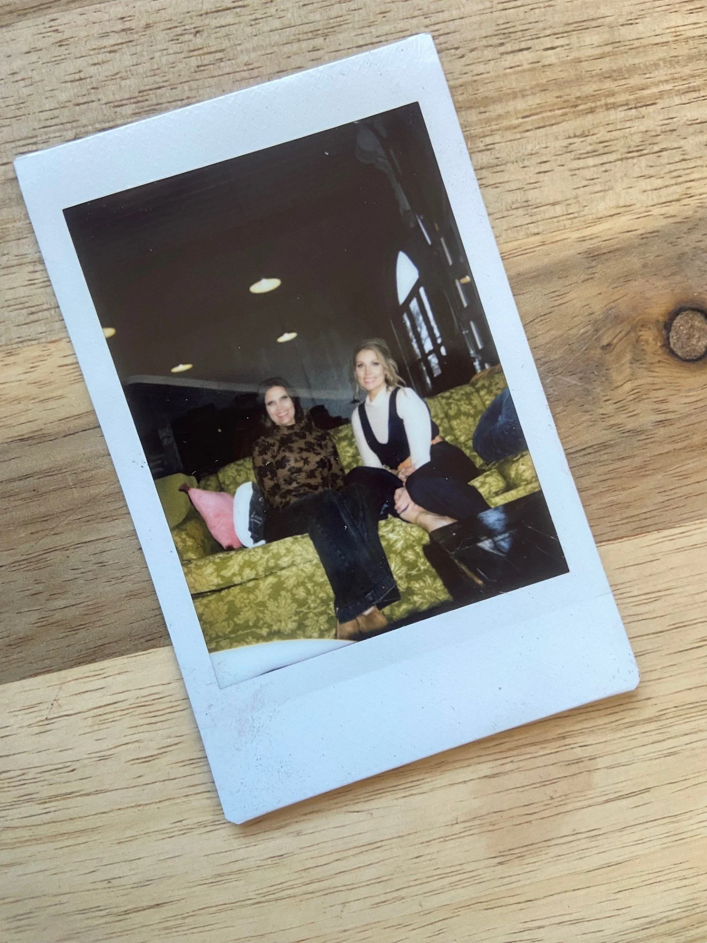 Two women sitting on a green patterned couch in a dimly lit room.