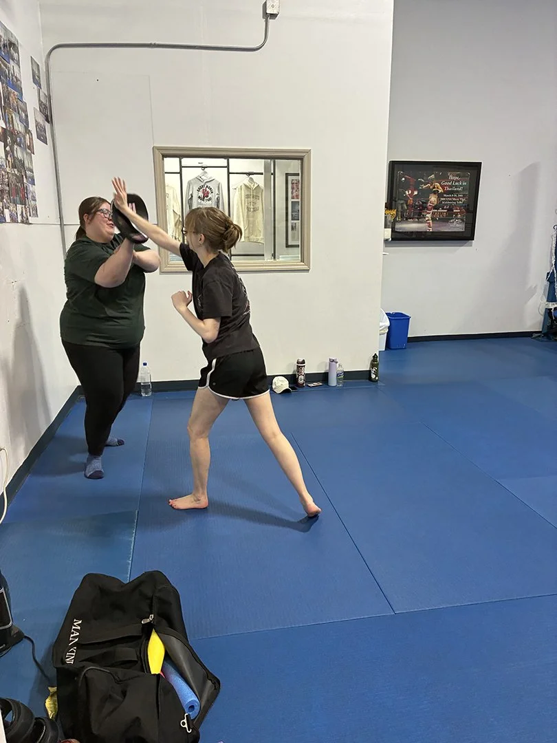 Two women practicing martial arts or kickboxing in a gym, one was wearing gloves, and the other is throwing a punch.