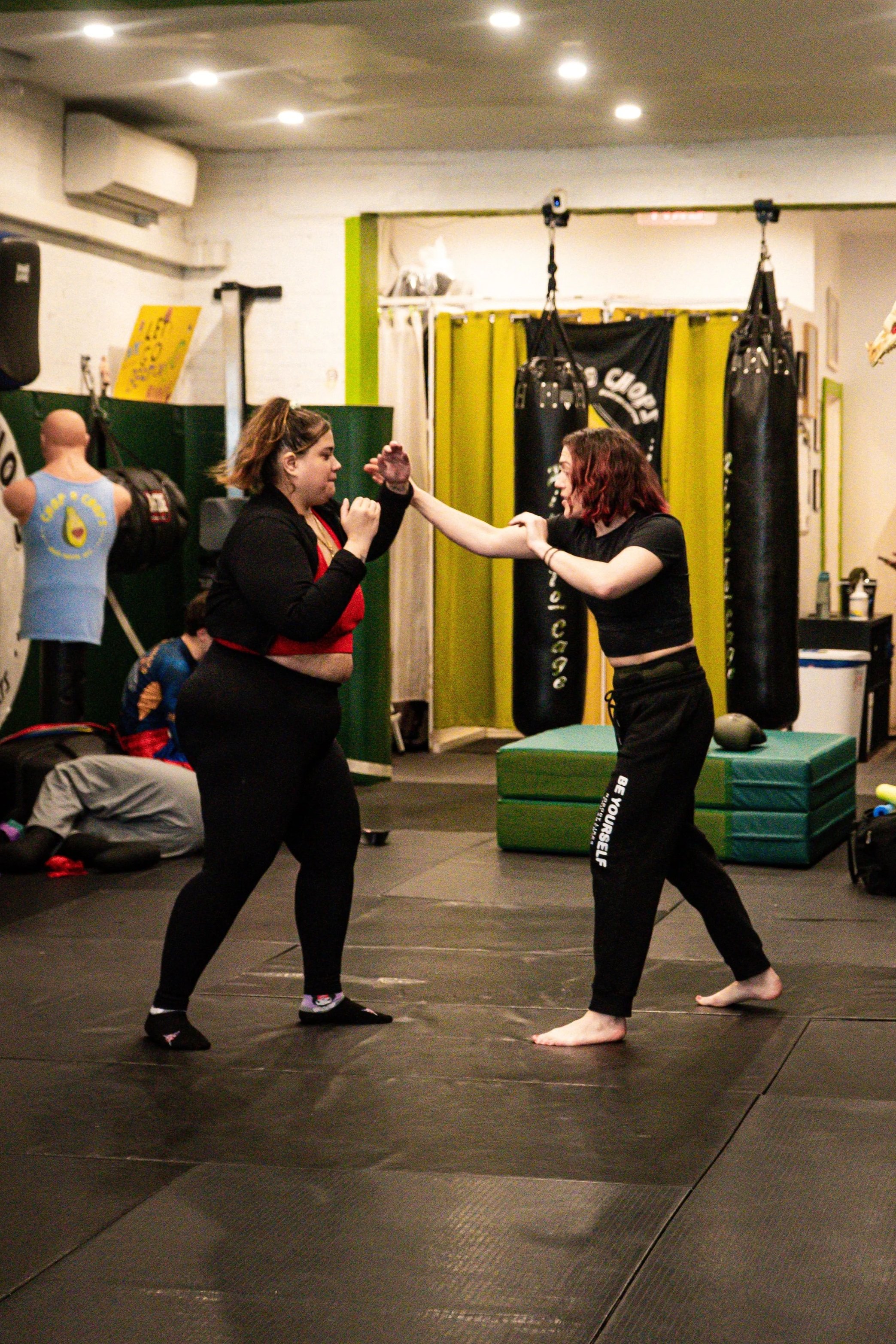High Kick's self-defense instructor, Rae Switlick, training a student at the Chop and Chops MMA gym in Brooklyn. Both are in fighting stance on a padded floor.