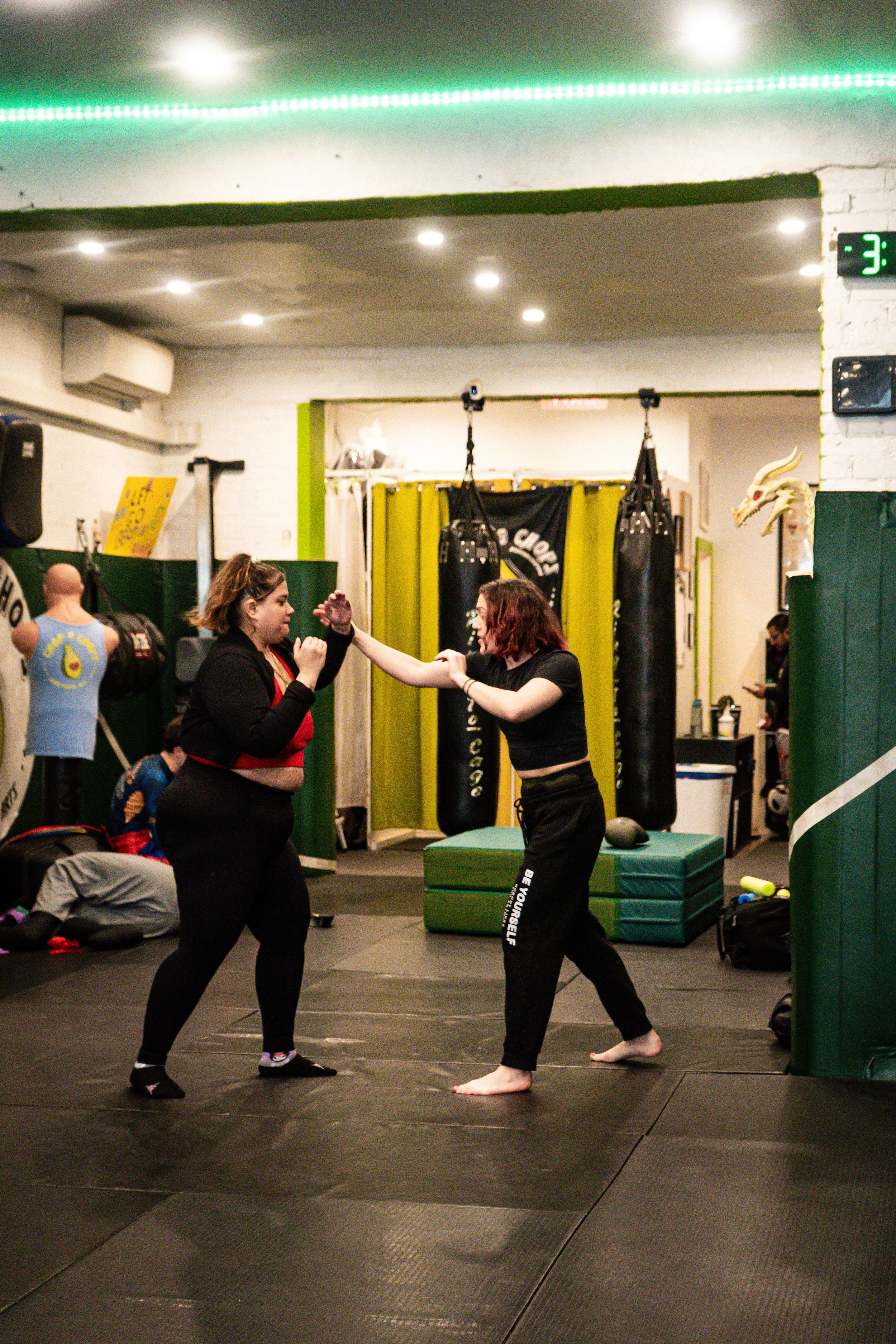 High Kick's self-defense instructor, Rae Switlick, training a student at the Chop and Chops MMA gym in Brooklyn. Both are in fighting stance on a padded floor.
