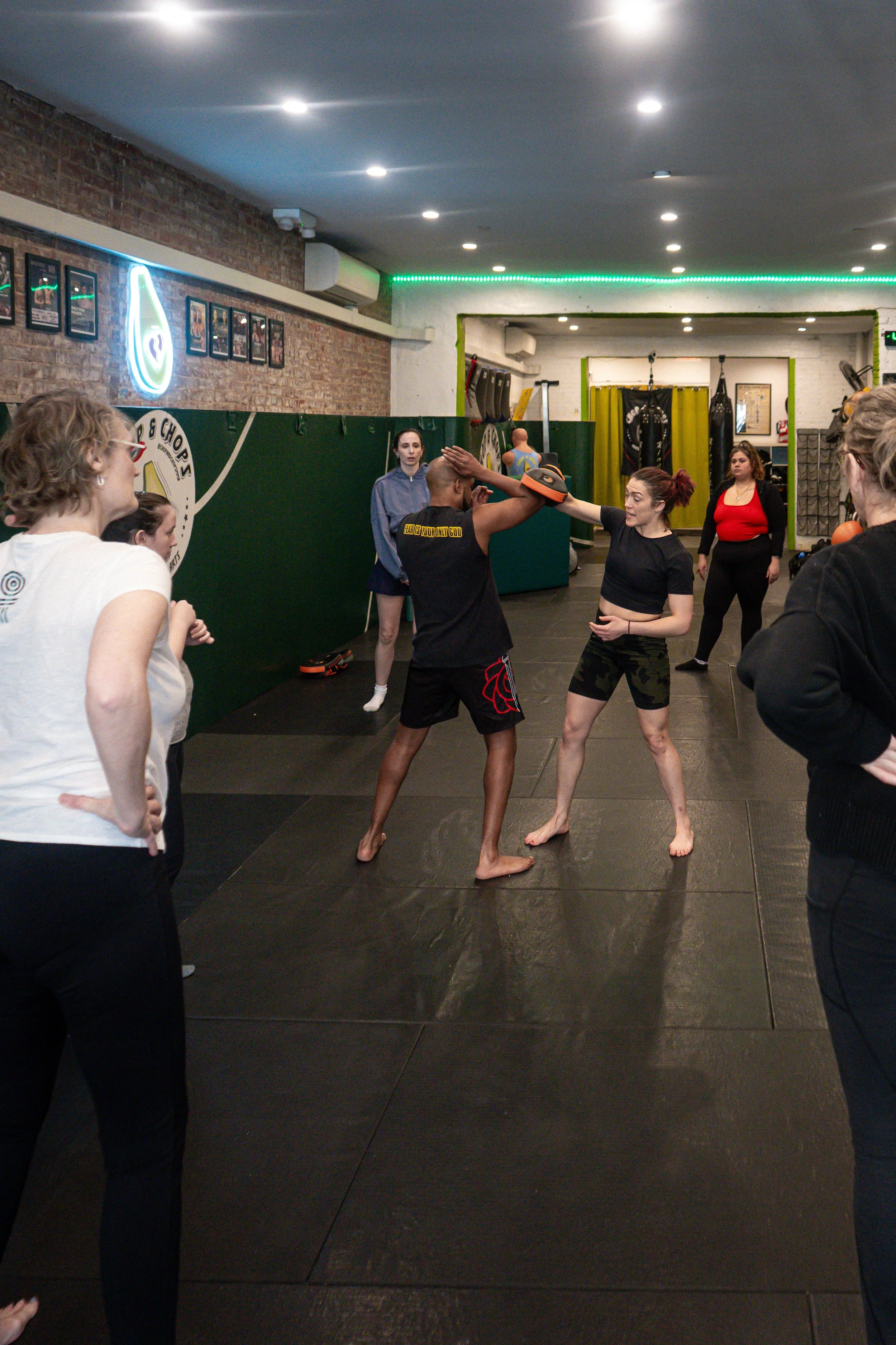 Students at the Chop and Chops MMA gym in Brooklyn practicing self-defense technique. Their instructor, Rae Switlick, demonstrates a move on one student while the others observe.