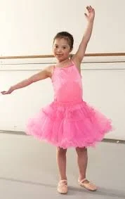Young girl in a pink ballet costume practicing ballet in a dance studio.