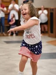 Young down syndrome girl smiling and dancing in a festive setting, wearing an Americana-themed outfit.