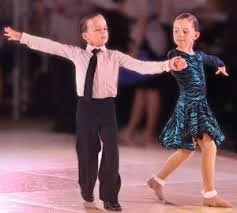 A young boy and girl ice skating together on an ice rink, holding hands with arms outstretched.