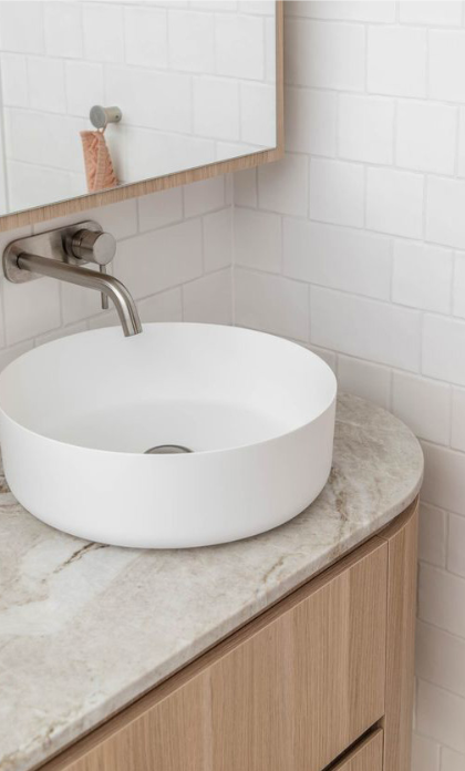 White vessel sink on a marble countertop in a bathroom with a wall-mounted faucet and a mirror above.