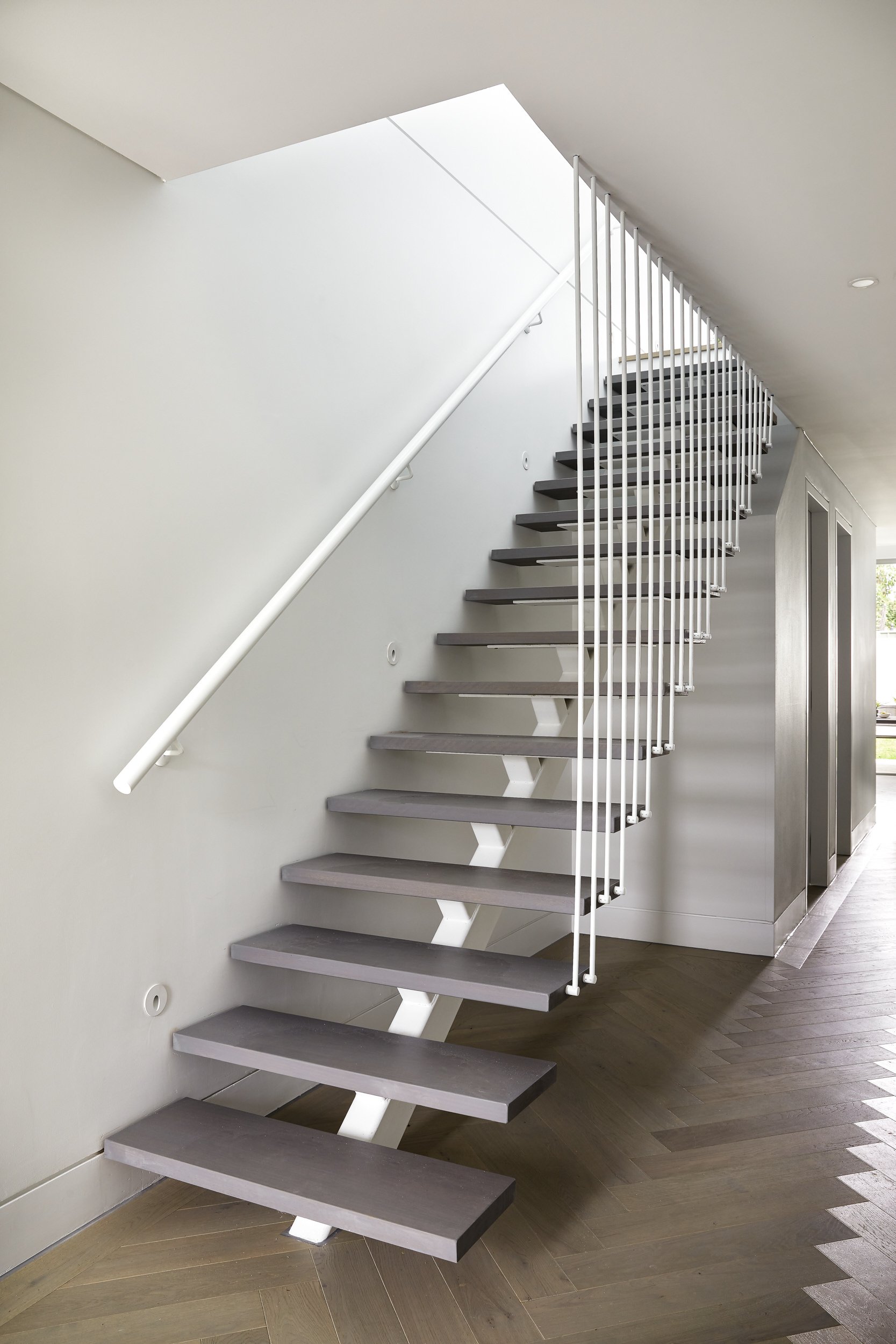 Modern staircase with floating dark-colored steps, white railing, and minimalist design in a well-lit interior.